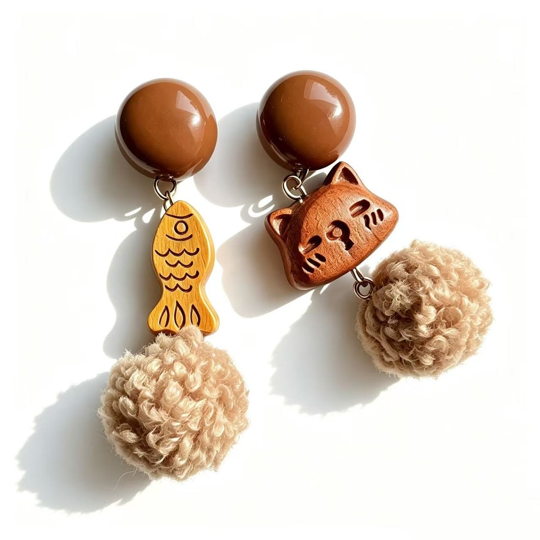Whimsical Cat and Fish Plush Drop Earrings: Pair of playful contemporary drop earrings featuring carved cat and fish motifs accented with soft plush pom-pom details. Fun novelty fashion accessory with mixed material design.