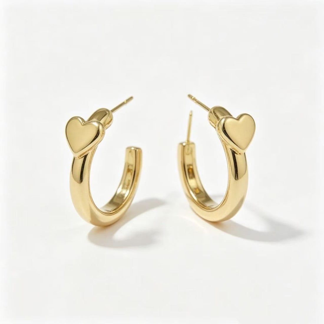 Gold-Gilded Heart Hoop Earrings: Pair of contemporary hoop earrings featuring a polished gold-gilded finish with heart-shaped accent details at the top of each hoop. Designed in a minimalist modern jewelry style suitable for