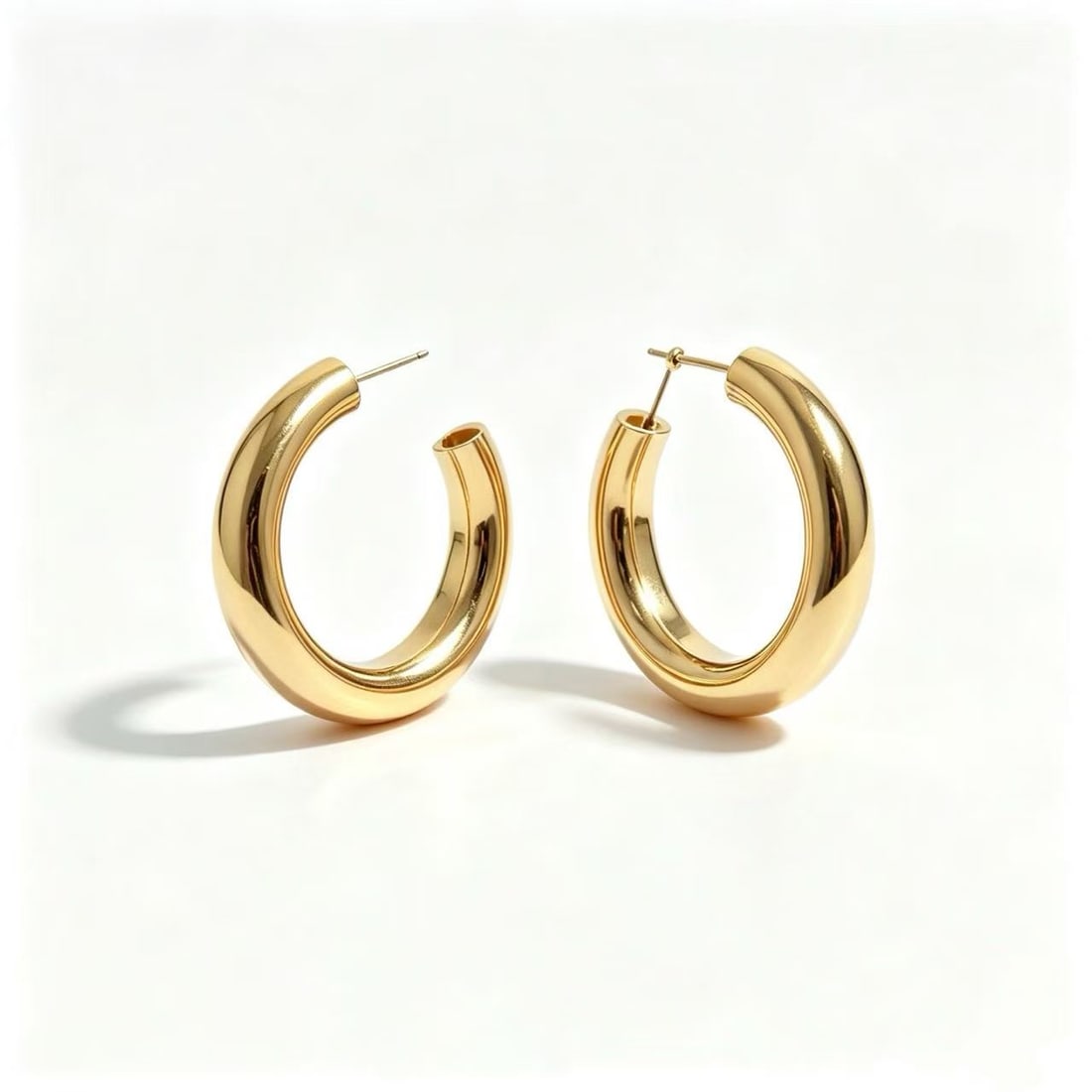 Gold-Gilded Oversized Hoop Earrings: Pair of contemporary oversized hoop earrings featuring a smooth rounded silhouette with polished gold-gilded finish. Minimalist modern design suitable for everyday wear or statement styling.
