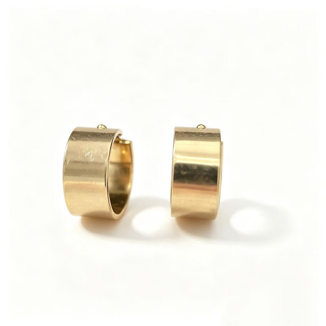 Gold-Gilded Wide Band Hoop Earrings: Pair of contemporary wide band hoop earrings featuring a smooth curved silhouette with polished gold-gilded finish. Bold minimalist design suitable for modern everyday styling or statement fashion