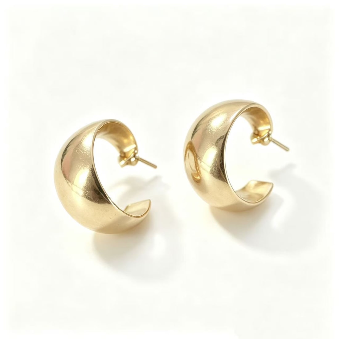 Gold-Gilded Wide Hoop Earrings: Pair of contemporary wide hoop earrings featuring a bold rounded silhouette with polished gold-gilded finish. Modern minimalist styling suitable for fashion wear, statement jewelry looks, or contempor