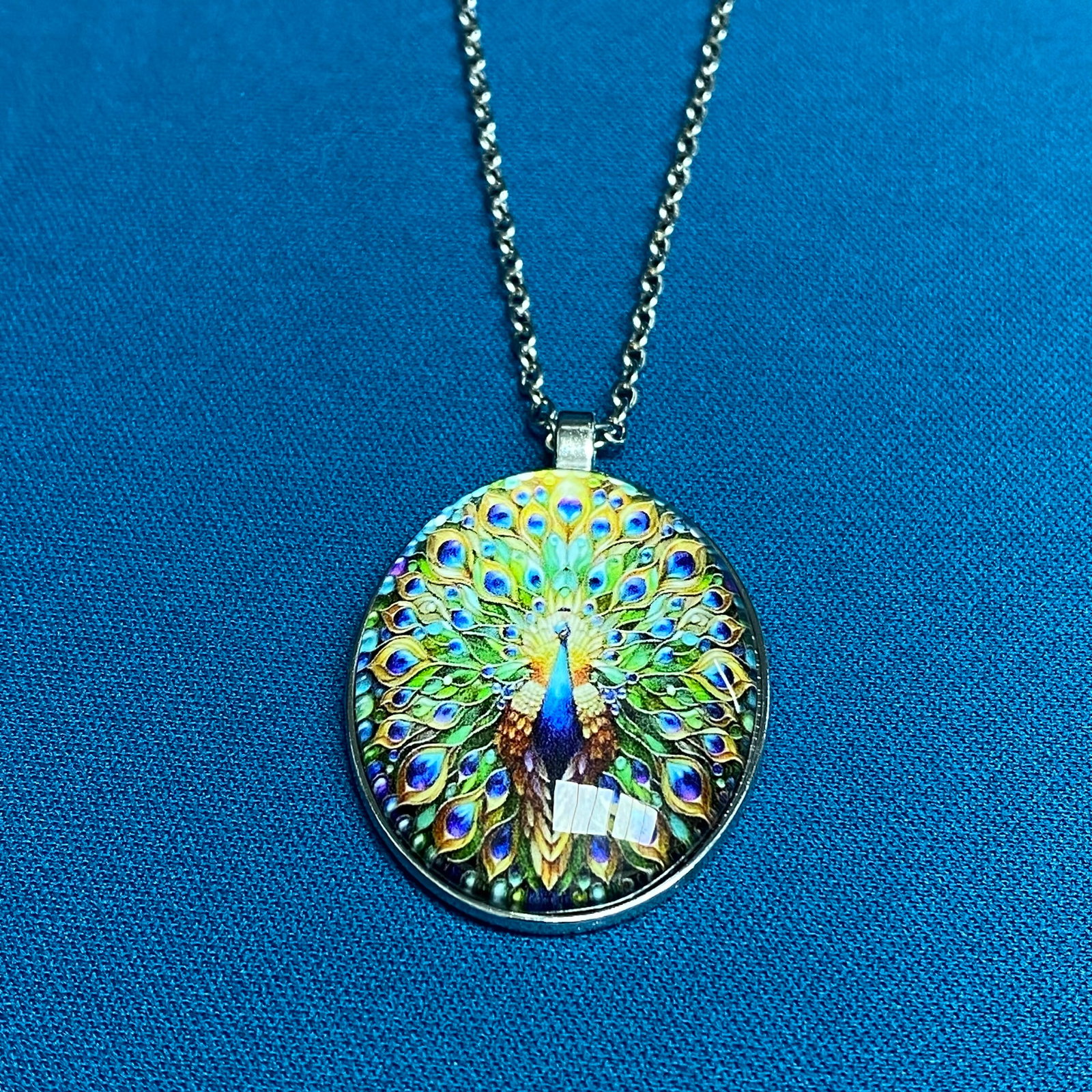 Vibrant Peacock Motif Glass Cabochon Pendant Necklace: This contemporary fashion pendant necklace showcases a highly detailed illustration of a majestic peacock with a fully fanned, colorful tail. The ornate, multi-colored graphic is protected beneath a s