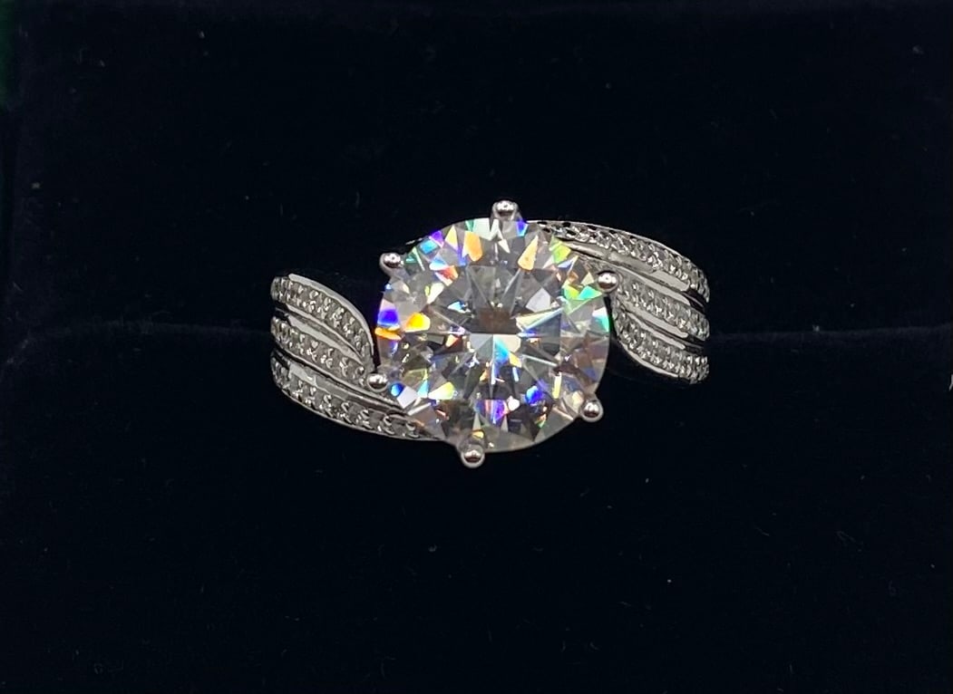5 Ct Round Moissanite Swirl Bypass Engagement Ring | 18K White Gold Plated 925 Silver: Featuring a fluid bypass design, this romantic solitaire ring wraps a round moissanite center stone in shimmering pavé-set accent ribbons. Finished in sleek 18K white gold plating over solid 925 ster