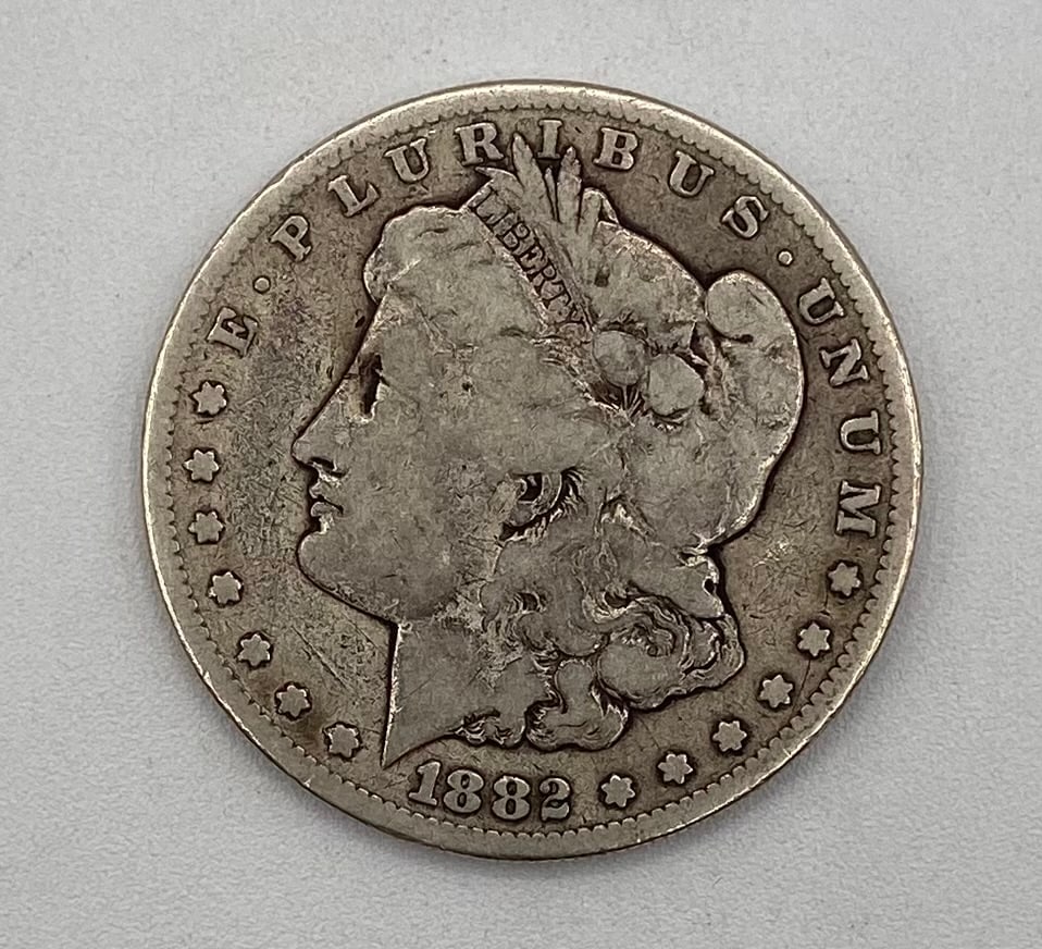 1882 Morgan Silver Dollar – Liberty Head: Design: Classic George T. Morgan Liberty head profile wearing a cap adorned with wheat and cotton blossom, surrounded by "E PLURIBUS UNUM" and 13 stars, dated 1882. Denomination: $1 USD Composition: 9
