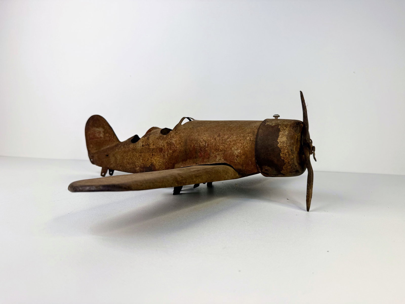 Vintage Pressed Steel Airplane: Vintage Pressed Steel Airplane showing significant rust, surface wear, and age-related patina throughout. Missing all tires, with condition reflecting years of use and storage. A solid restoration can