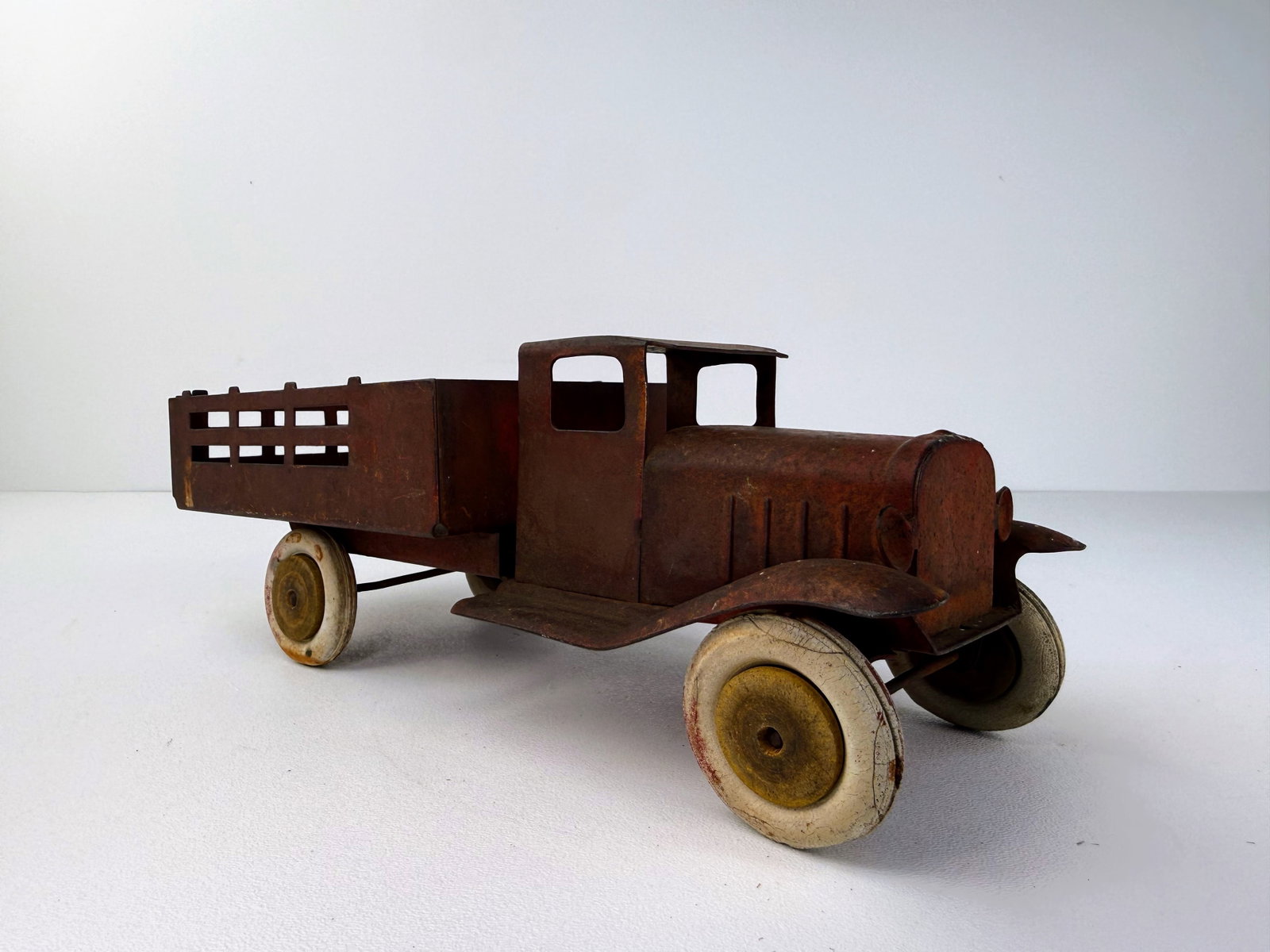 Wyandotte Pressed Steel Vintage Stake Bed Toy Truck: Wyandotte pressed steel vintage stake bed toy truck. A classic early toy with an attractive original patina and four original wooden wheels, with the rear wheels loose. Shows heavy rusting consistent 