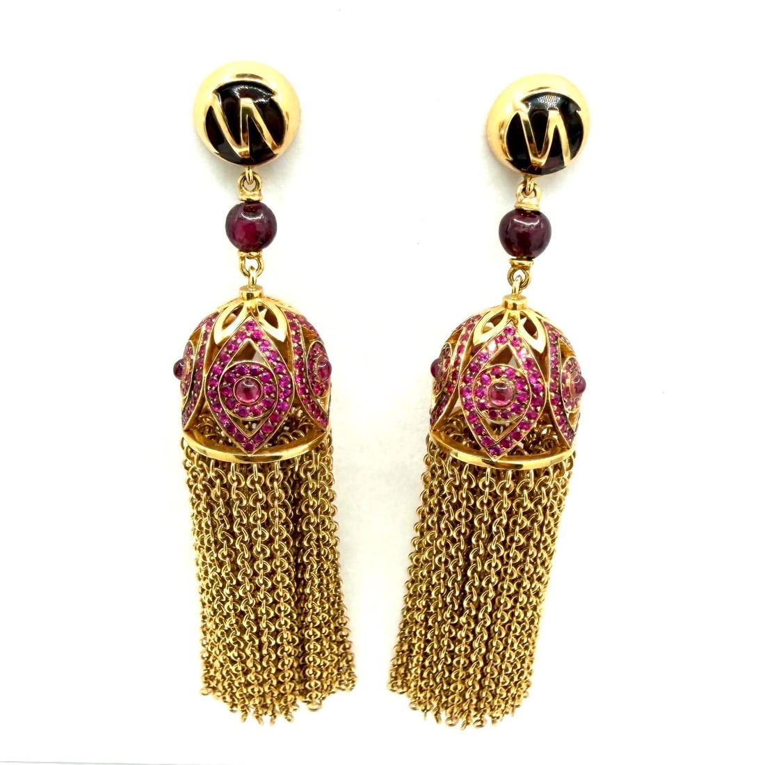 Art Deco Style 18kt Yellow Gold Dangle Chain Tassel Pair of Earrings With Rubies: Design: The earrings feature an ornate, bell-shaped drop with an intricate open design resembling an evil eye or a stylized flower, set with multiple rubies. Materials: They are crafted in 18kt. Yello