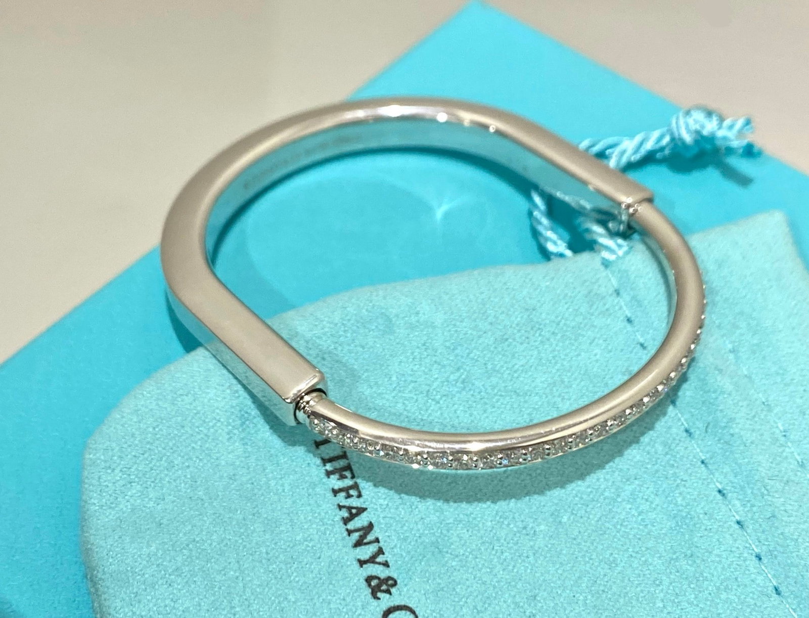 Tiffany Lock Bangle in White Gold with Half Pavé Diamonds: Condition: Like New Brand: Tiffany & Co. Material: 18k White Gold GemStone: Diamond Carat Weight: 1.20 TCW Stone Shape: Round-cut Size: Medium, 17 Comes with an original box or pouch.