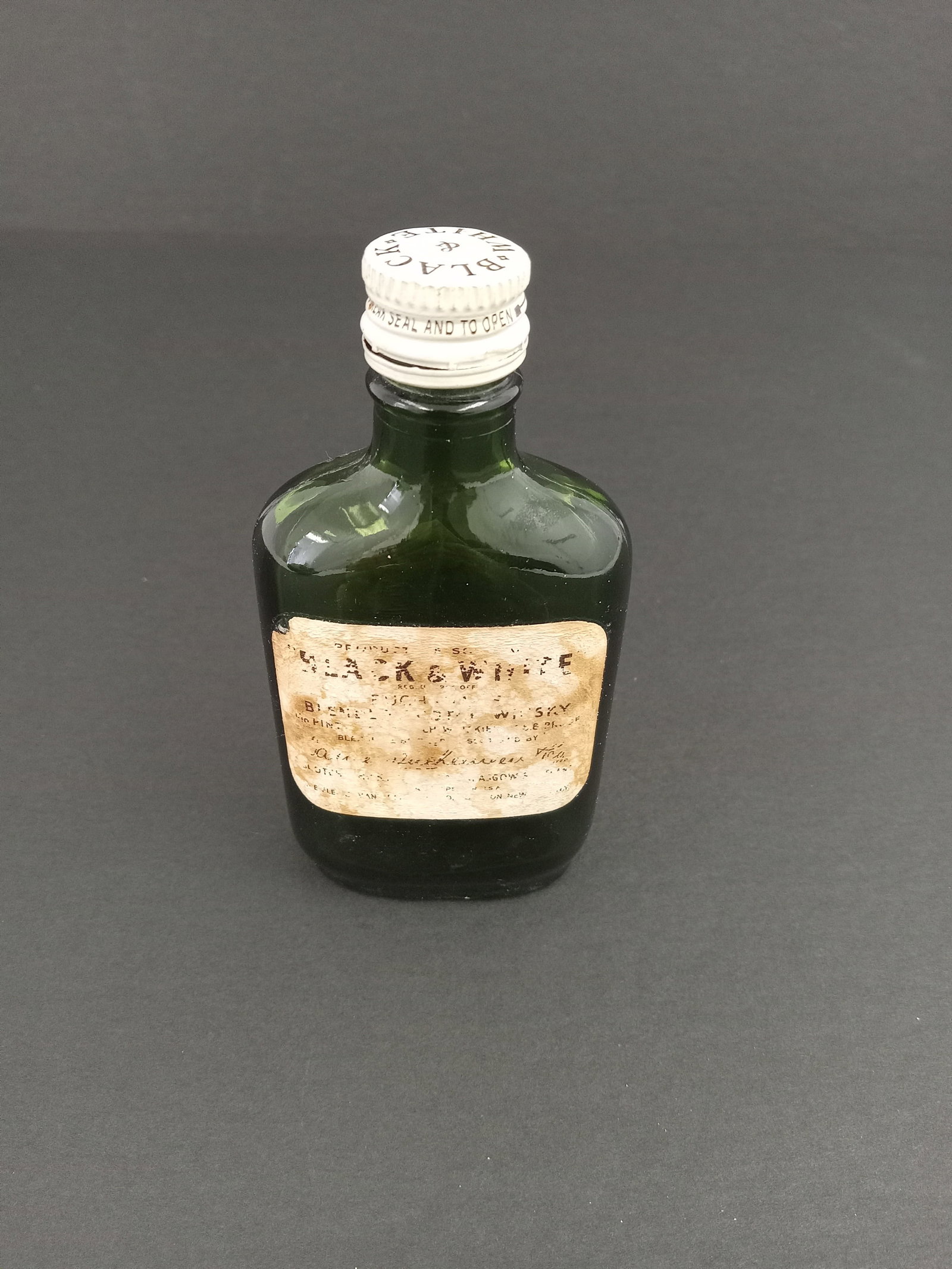 Vintage Mini Green Glass Bottle of Black and White Whiskey: Mini or sample size bottlle of Black and White whiskey with cap. Antique Scotish Whiskey. These are part of the estate sale and we do not have a COA. All lots offered in our auctions are sold strictly