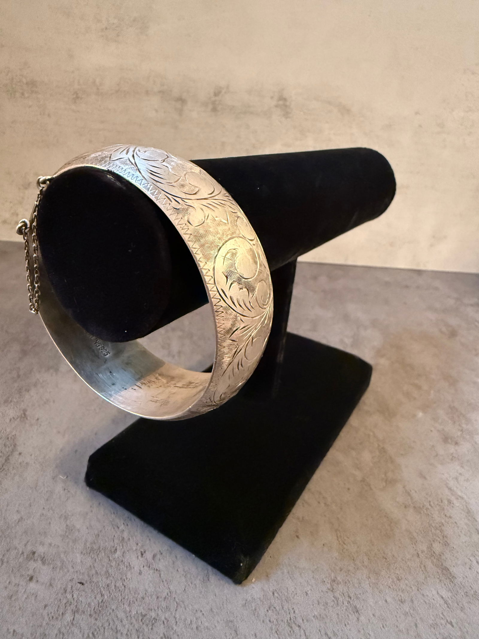 Sterling silver Hinged Bangle Bracelet with Safety Chain: Sterling silver bangle bracelet of hinged construction, the exterior finely engraved with scrolling foliate and geometric decoration. Fitted with a concealed clasp and an attached safety chain for add