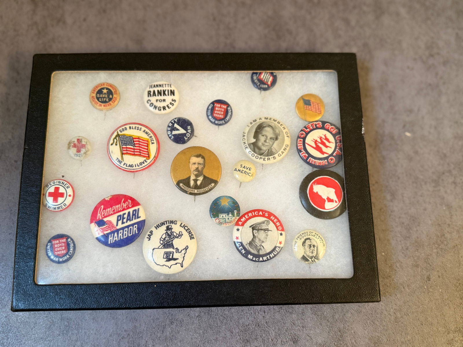 Framed Collection of Vintage American Political & Patriotic Pinback Buttons: A framed display of assorted vintage American pinback buttons featuring a mix of political, patriotic, and wartime themes.The collection includes examples with imagery and slogans such as:Theodore