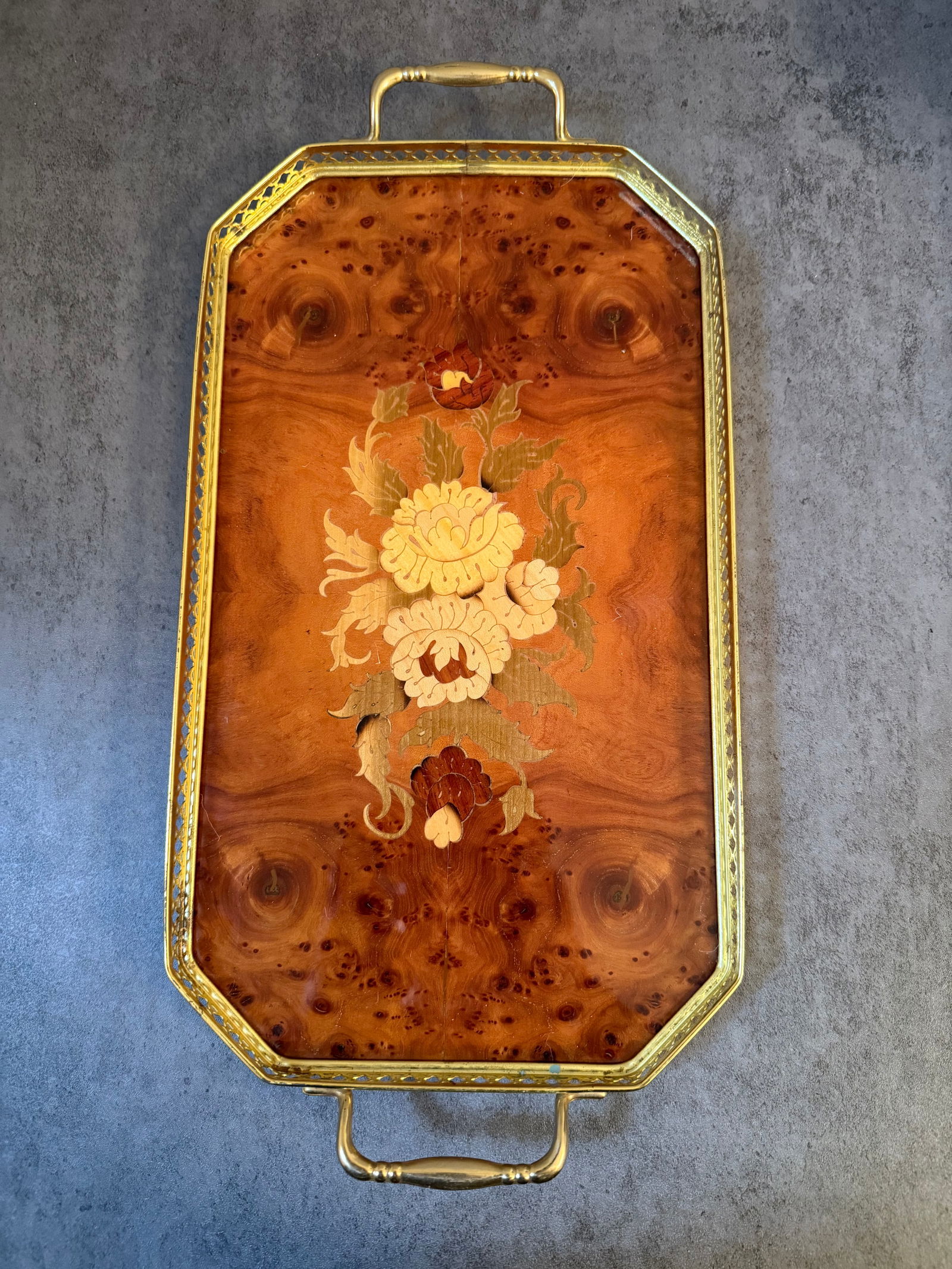 Decorative Burlwood-Style Serving Tray with Floral Inlay & Brass Handles: A decorative rectangular serving tray featuring a burlwood-style veneered surface with an elegant floral marquetry-style inlay at center. The tray is framed with a pierced brass-tone gallery rim and