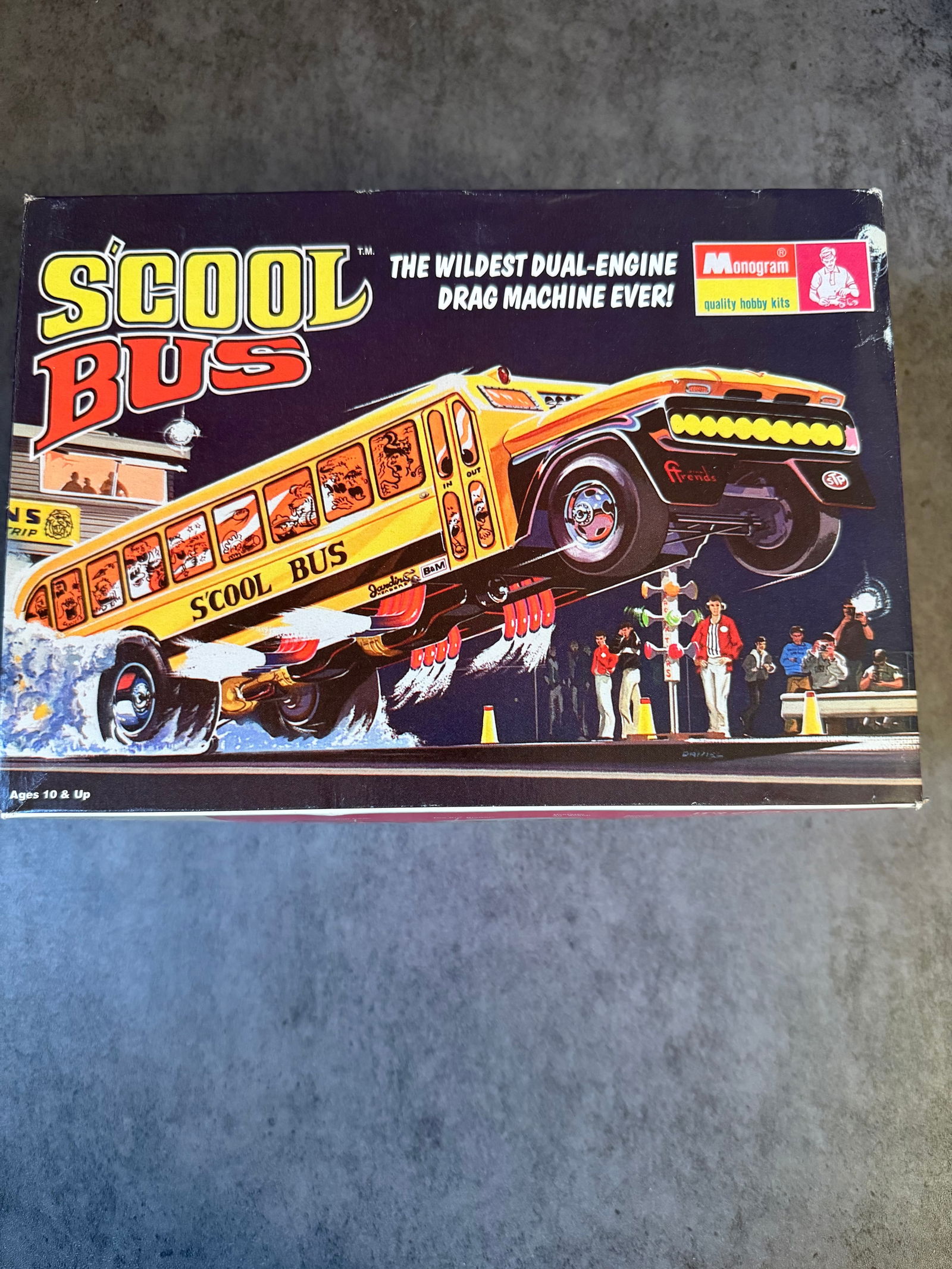Monogram “School Bus” Dual-Engine Drag Machine Model Kit: A boxed Monogram plastic model kit titled “School Bus – The Wildest Dual-Engine Drag Machine Ever!”, depicting a custom hot-rod style school bus drag racer.The kit includes molded plastic