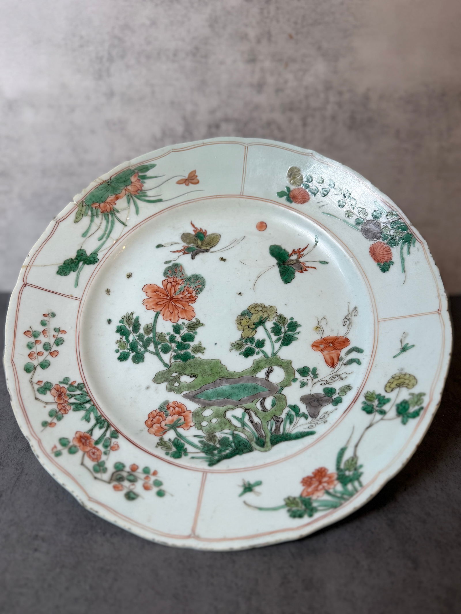 Chinese Export Famille Verte Porcelain Plate, Qing Dynasty: A Chinese export porcelain plate decorated in famille verte enamels, featuring butterflies, flowers, scholar’s rock, and garden scene motifs. The cavetto is finely painted with floral sprays and but