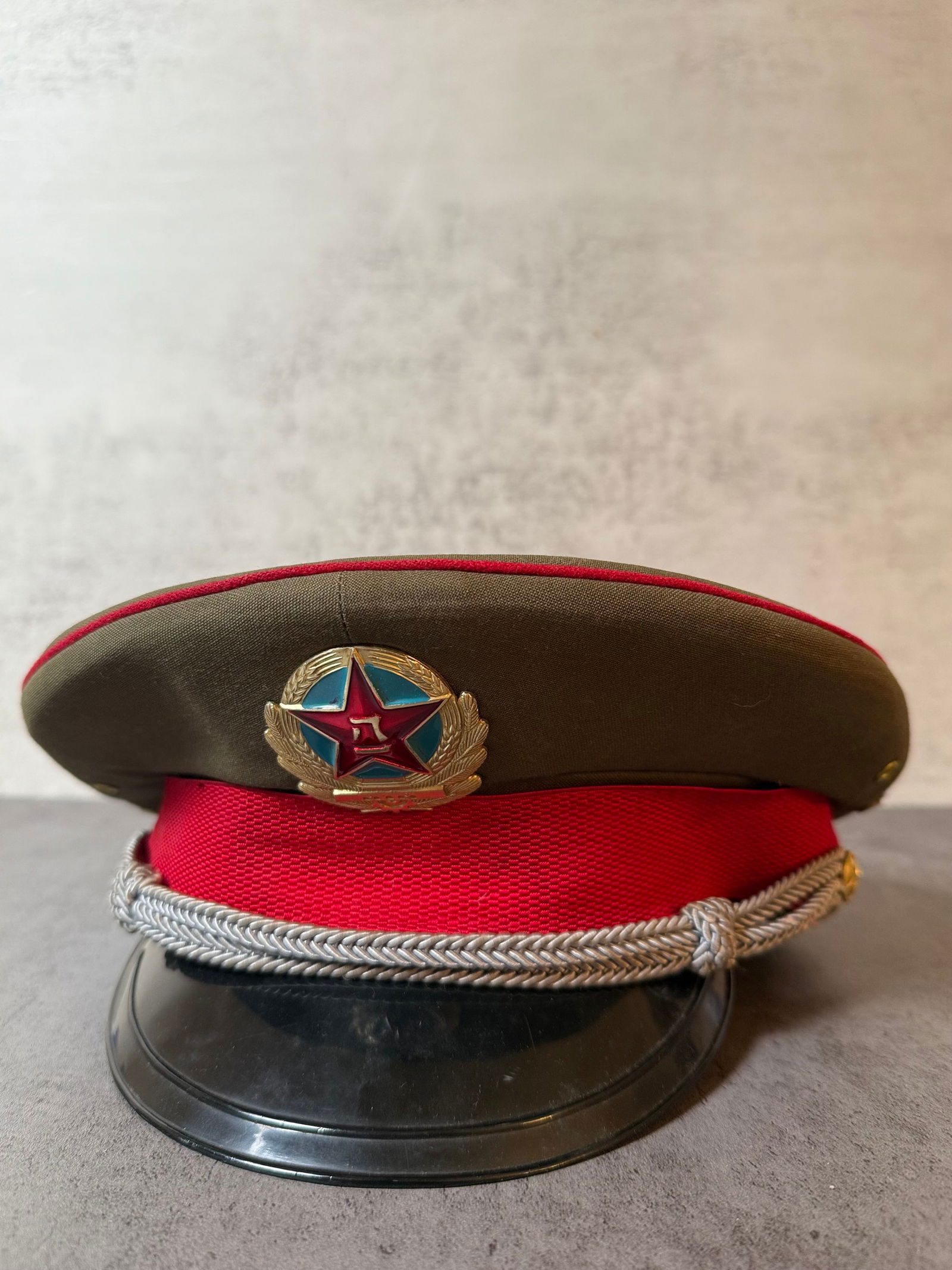 Chinese Military Dress Cap with Red Band & Enamel Star Emblem: Chinese military-style dress cap featuring an olive-green wool body accented with red piping and a bold red band. The front displays a metal and enamel five-pointed star emblem, symbol of the People��