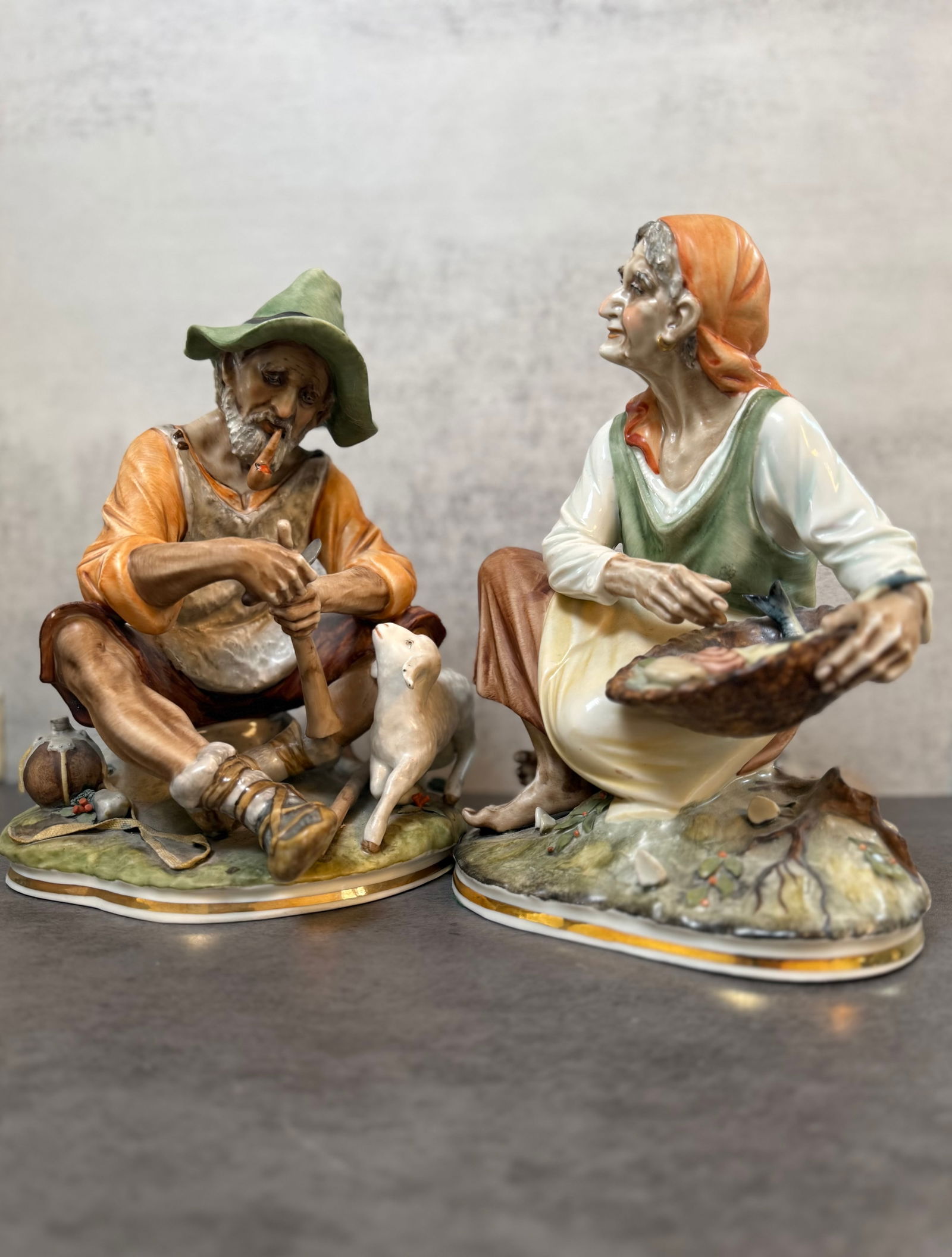 Pair of German Sandizell Porcelain Peasant Figures, 20th Century: A pair of German Sandizell porcelain figures depicting a seated peasant man with a pipe and dog, and a seated peasant woman holding a basket, each naturalistically modeled and polychrome decorated