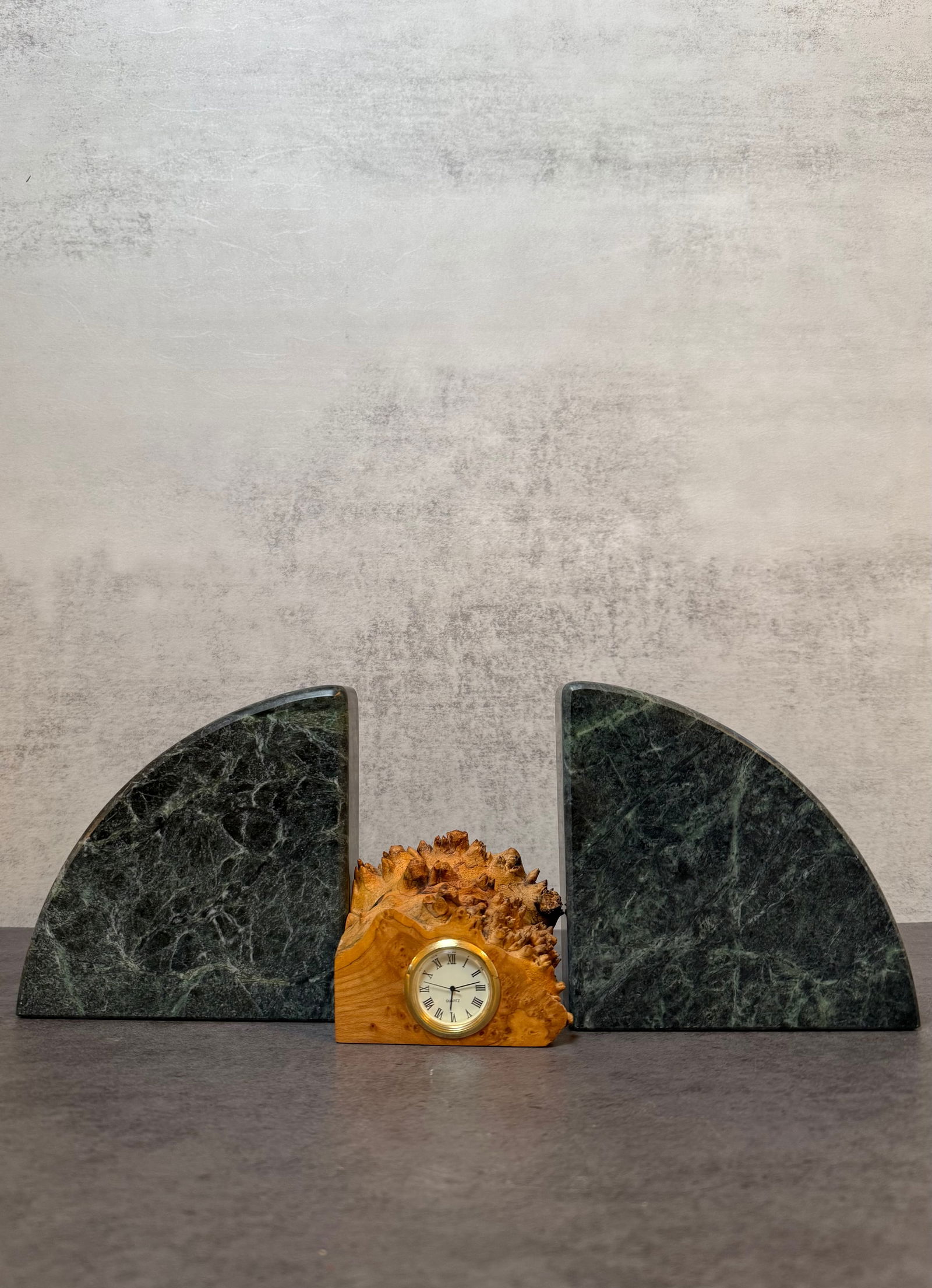 Pair of Green Marble Arch Form Bookends Together with a Burl Wood Desk Clock: A pair of green marble arch form bookends together with a small burl wood desk clock with brass bezel and Roman numeral dial. Bookend height approximately 5 inches; clock height approximately 3 inches