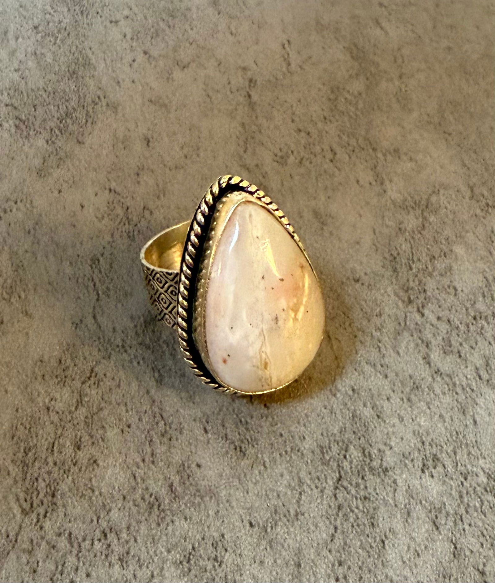Silver Tone and Pear-Shaped Cabochon Stone Cocktail Ring, Size 7: A silver tone cocktail ring set with a large pear-shaped cabochon stone in cream and blush tones with natural inclusions, within a twisted rope border setting and engraved geometric band. Ring size