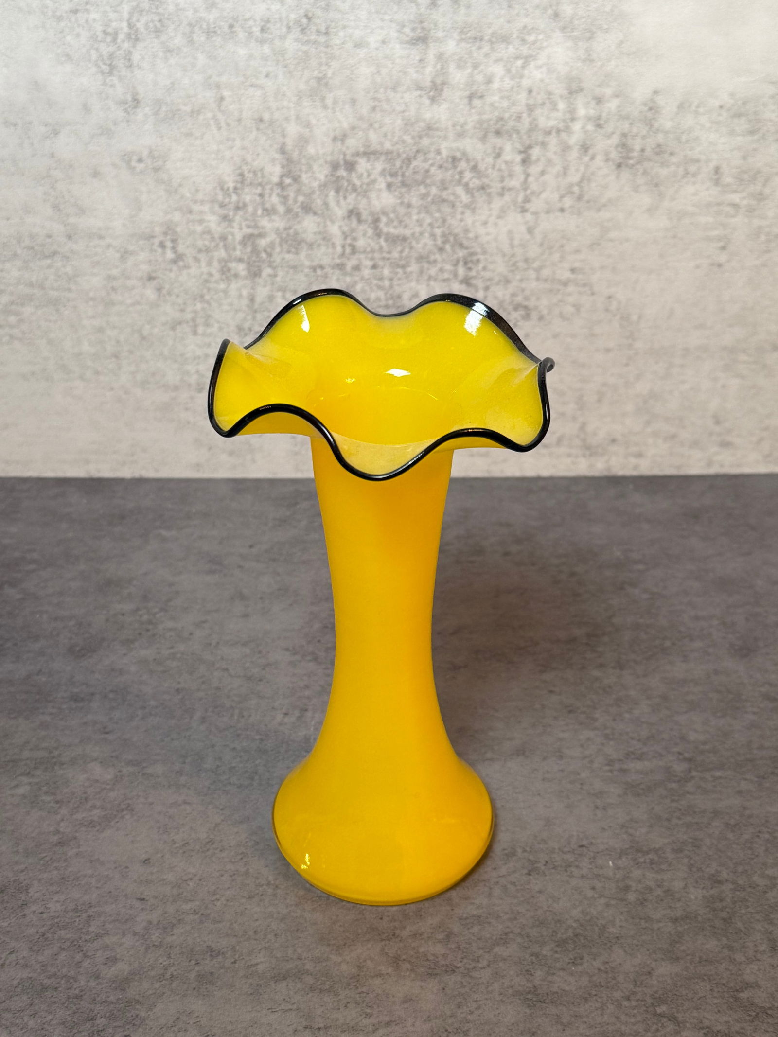Yellow Art Glass Vase with Black Ruffled Rim: A decorative yellow art glass vase featuring a flared ruffled rim with contrasting black edge. Trumpet form body suitable for decorative display.