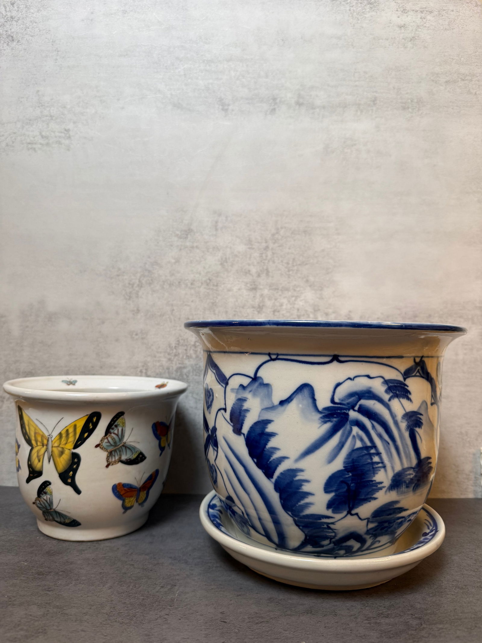 Decorative Porcelain Planter Group with Drainage Holes: A group of two decorative porcelain planters including one blue and white example with undertray and one butterfly decorated planter. Both with drainage holes.