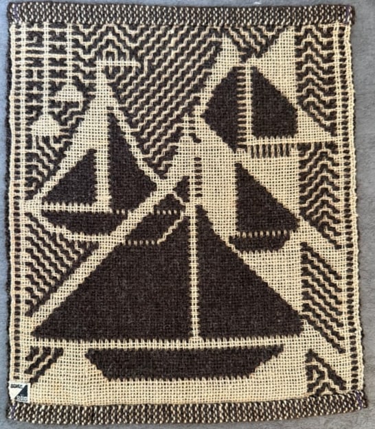 Vintage Hand Embroidered Needlepoint Textile Panel with Sailing Boat Motif: A vintage hand-embroidered needlepoint textile panel featuring a stylized sailing boat design within a geometric patterned border. The piece is worked in dark brown wool thread on an open canvas