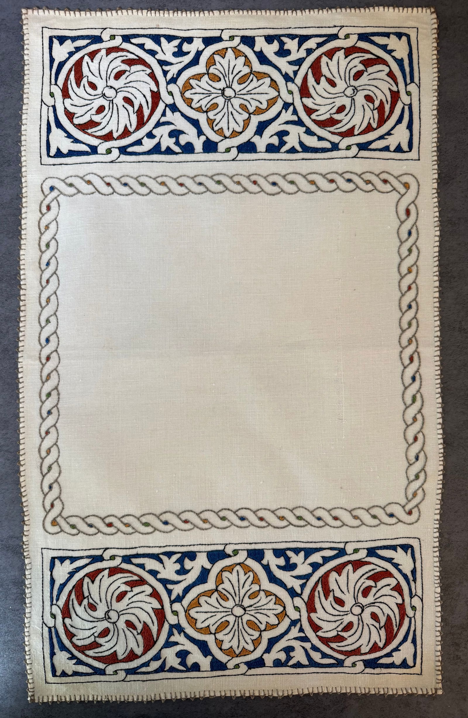 Vintage Hand Embroidered Linen Table Mat with Decorative Tile Motif: A vintage hand-embroidered linen table mat featuring decorative scroll and medallion motifs reminiscent of Mediterranean or Spanish tile designs. The embroidery is worked in multiple colors including