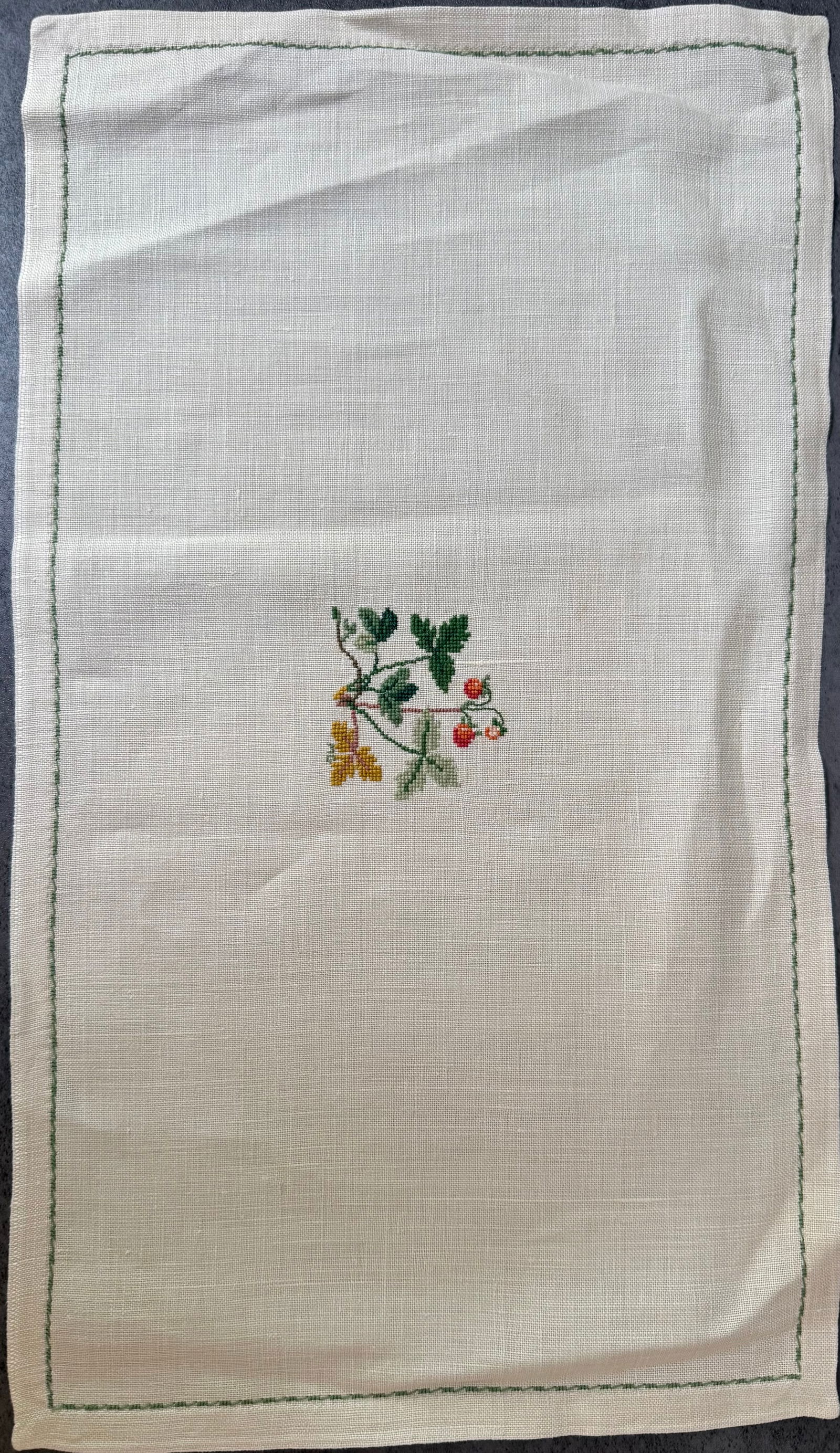 Vintage Hand Embroidered Linen Table Mat with Floral Motif, 17 x 9 in: A vintage hand-embroidered linen table mat featuring a delicate floral motif embroidered in colored thread at the center. The design is set within a simple stitched green border on natural linen