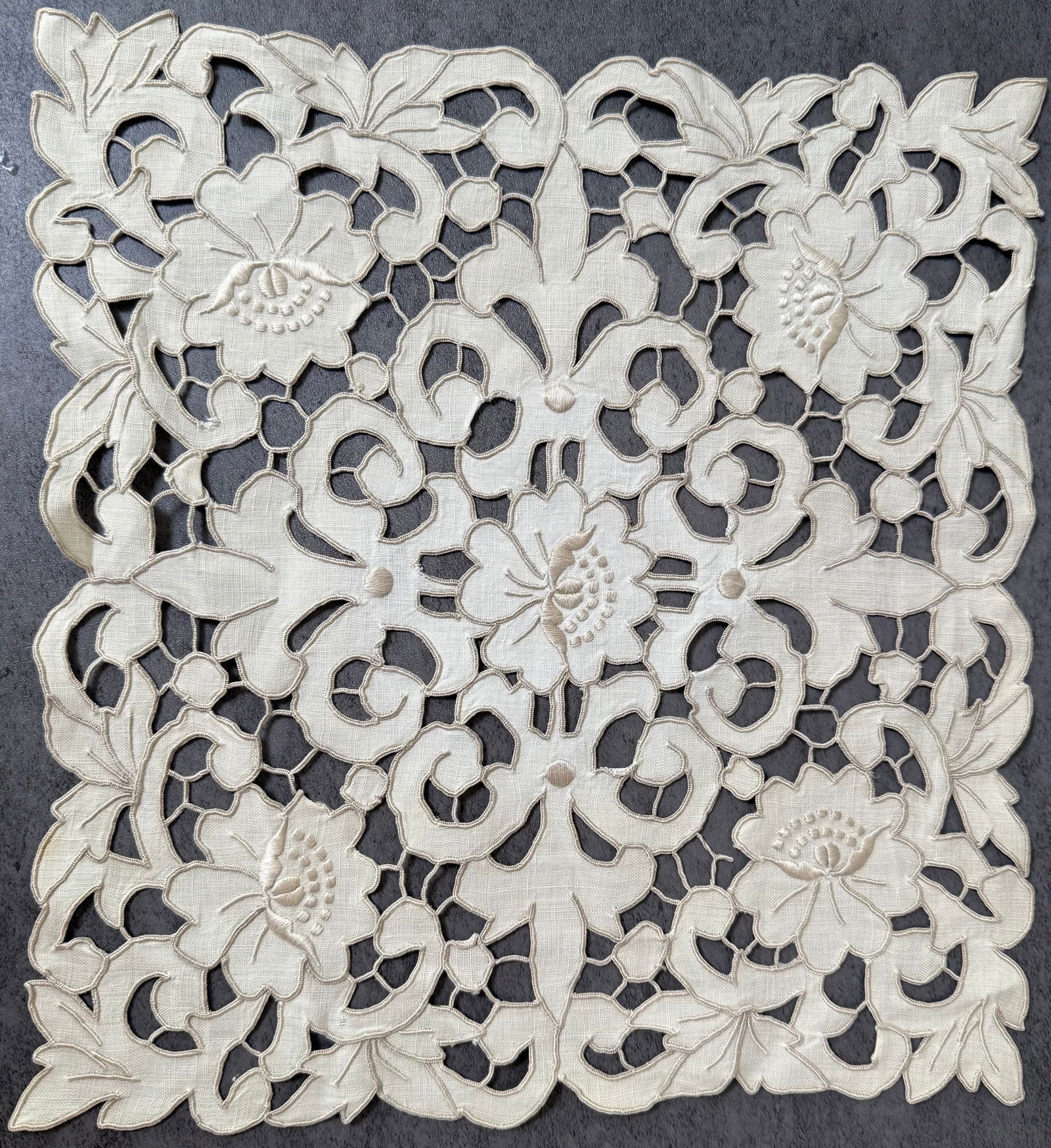 Vintage Hand Embroidered Cutwork Linen Table Topper with Floral Design: A vintage hand-embroidered linen textile featuring elaborate cutwork embroidery forming an openwork floral and scrolling vine design. The symmetrical composition displays stylized blossoms and