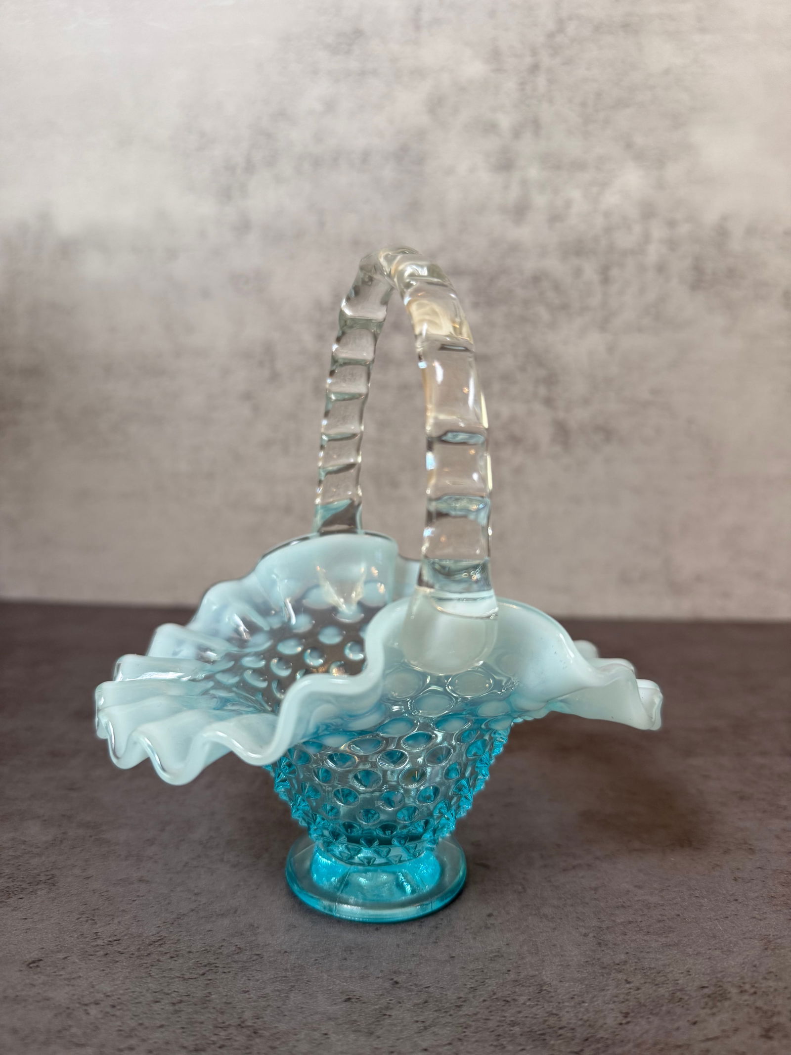 Opalescent Hobnail Glass Basket: Decorative opalescent glass basket featuring a hobnail pattern body, ruffled rim and applied clear glass handle. Light blue translucent glass with milky opalescent tone. Approx. 6 in H x 5 in W.