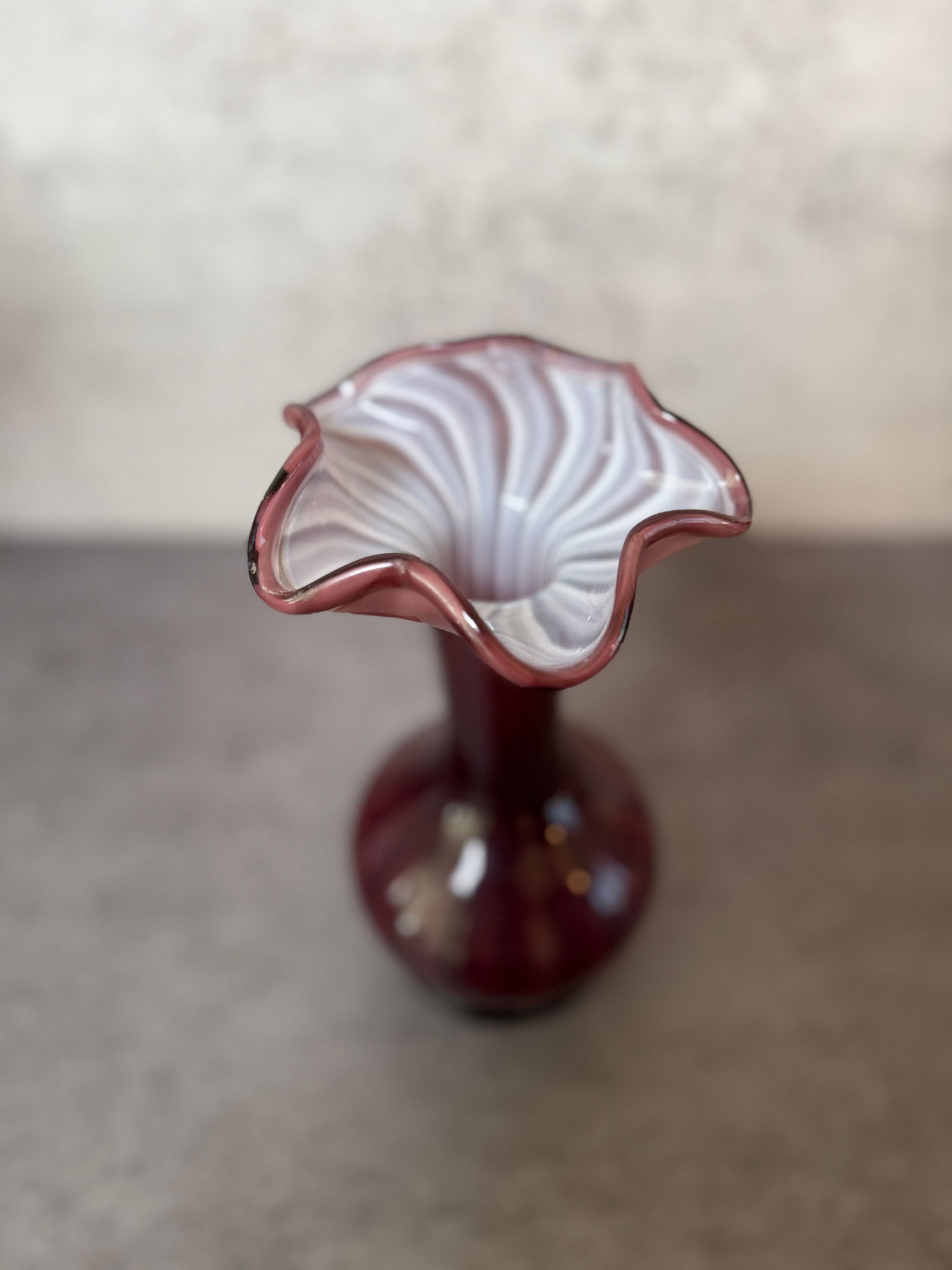 Murano Style Red Swirl Art Glass Vase: Decorative art glass vase featuring a deep red body with white interior swirl pattern and a ruffled rim. Bulbous base with a tall slender neck. Approx. 9 in H x 5 in W.
