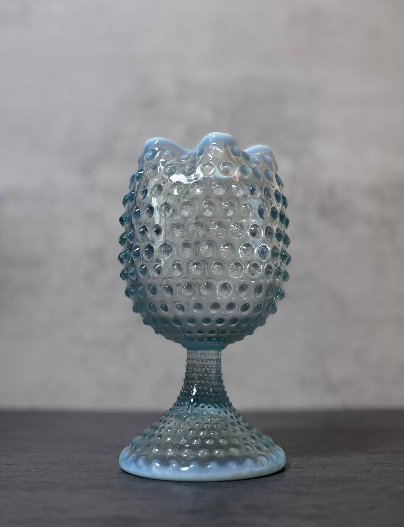Opalescent Hobnail Glass Pedestal Vase: Decorative opalescent glass pedestal vase featuring an overall hobnail pattern with a scalloped and ruffled rim. The bowl form body rises above a short textured stem and circular foot, all molded with