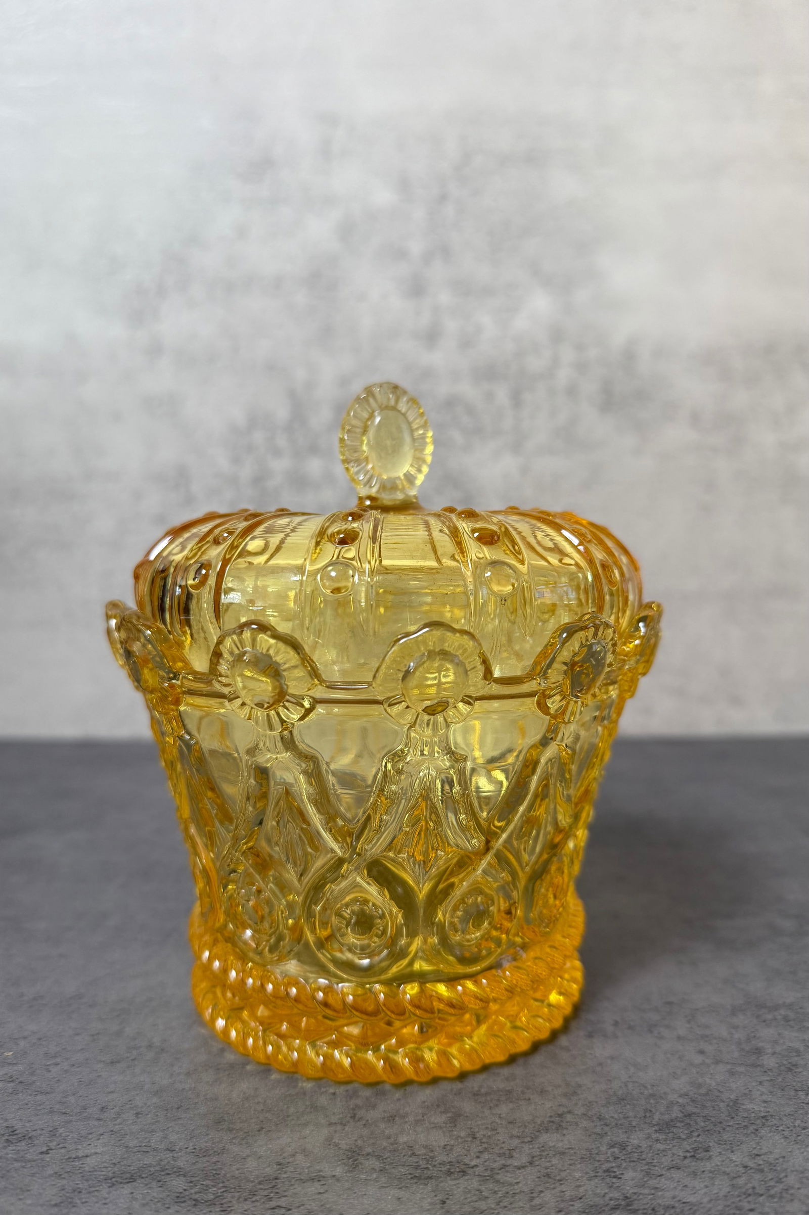 Amber Pressed Glass Covered Candy Dish: Decorative amber pressed glass covered dish featuring a domed lid with molded radial panels and a small oval finial. The body is richly decorated with raised floral and ribbon motifs in relief, above