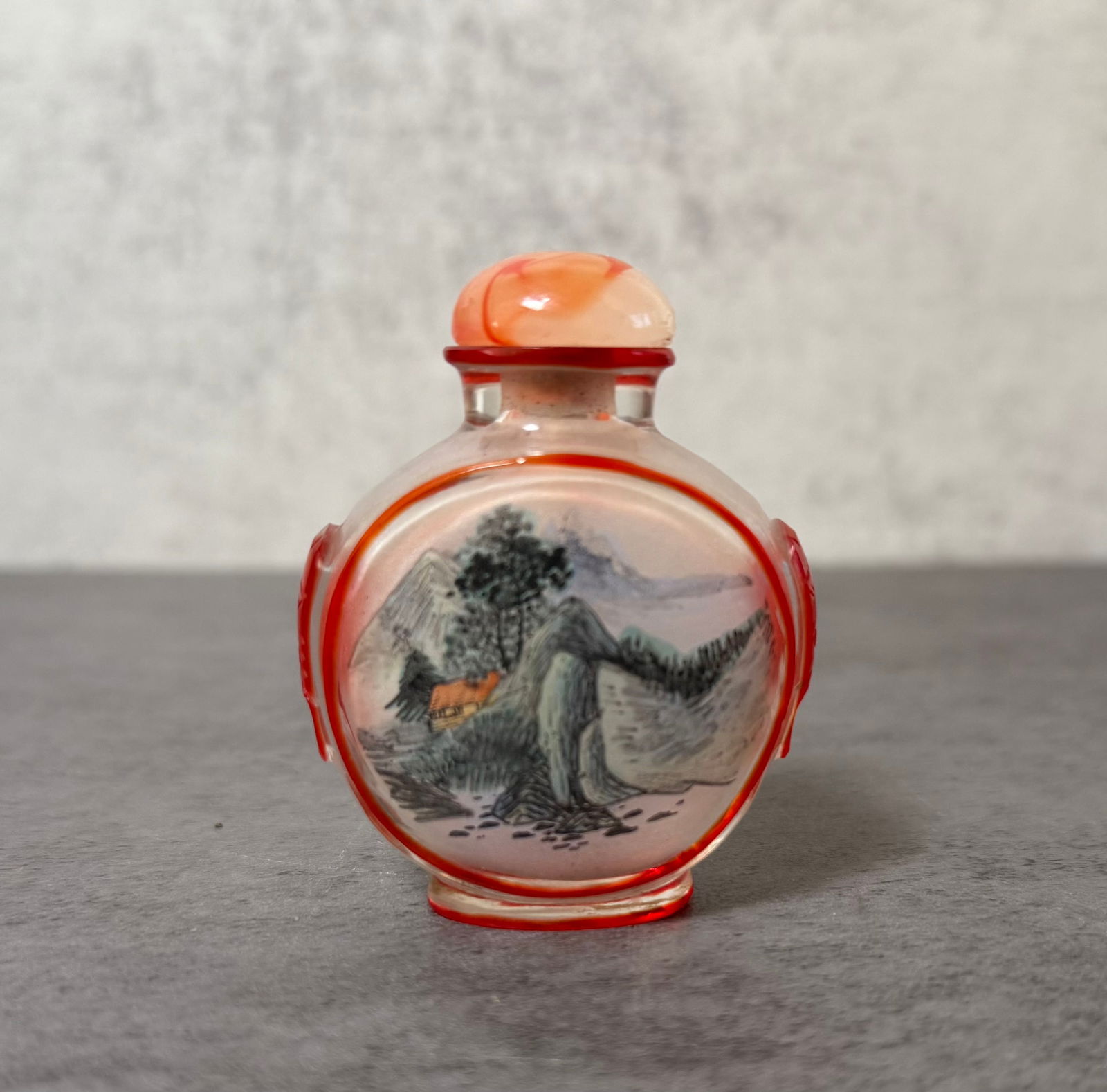 Chinese Overlay Glass Inside Painted Snuff Bottle with Landscape: Chinese inside-painted glass snuff bottle of rounded form with red overlay decoration around the sides and border. The interior painting depicts a traditional Chinese mountain landscape with a small