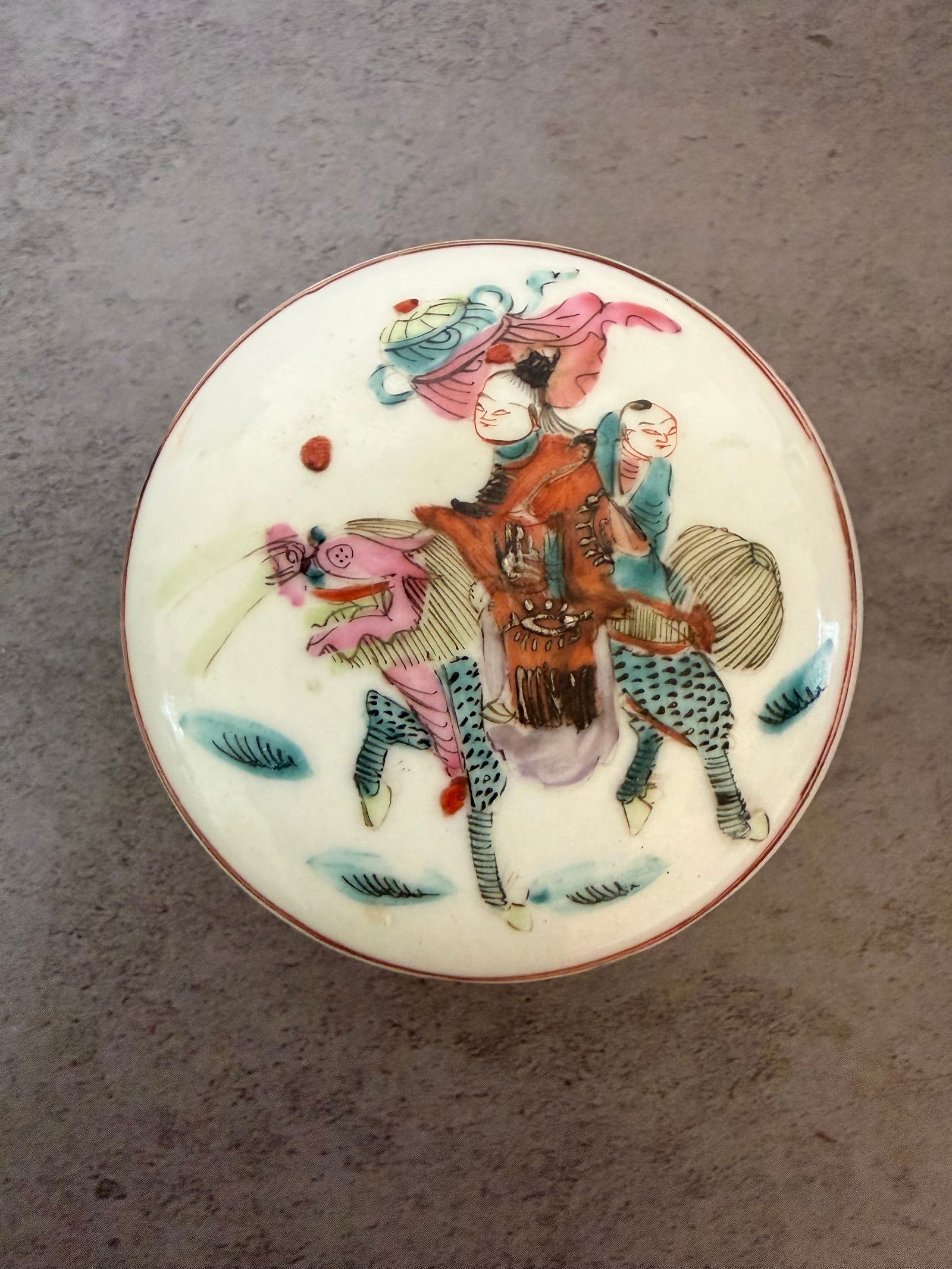 Chinese Porcelain Covered Box with Figural Decoration, 20th Century: Chinese porcelain covered box decorated to the lid with a figural scene of a rider accompanied by attendants in a stylized landscape. The sides with simple floral motifs and the rim outlined in iron