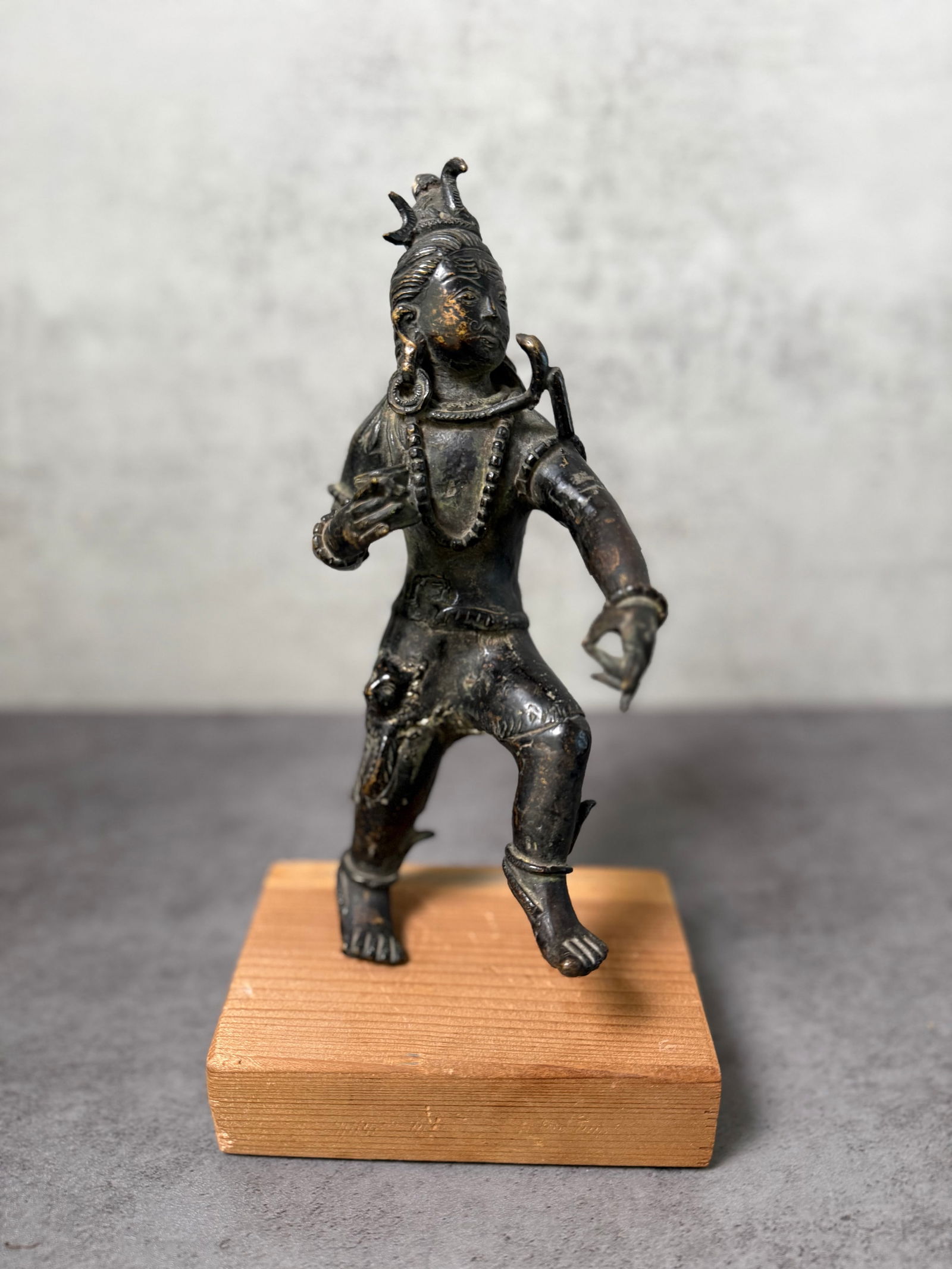 Antique Indian Style Bronze Dancing Shiva Figure on Stand: Expressive bronze figure depicting a dancing deity in the style of Shiva Nataraja, shown in a dynamic posture with one leg raised and arms extended in graceful motion. The figure wears traditional