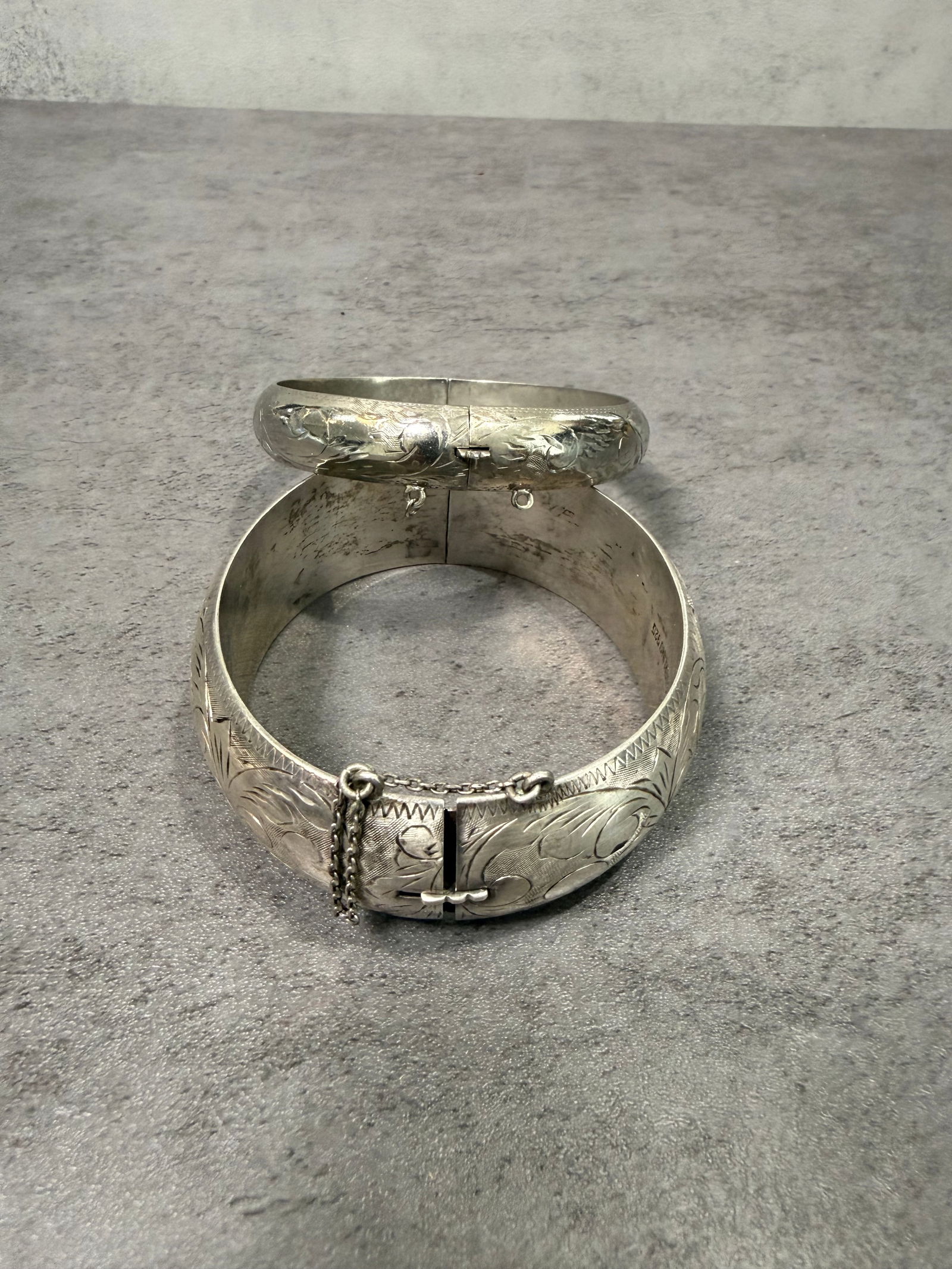 Vintage Sterling Silver Hinged Bangle Bracelets, Engraved Floral Motif, Clasp Closure, Set of Two: A charming set of two vintage sterling silver bangle bracelets featuring classic hinged construction with secure clasp closures. One bracelet is decorated with delicate engraved floral scroll motifs,