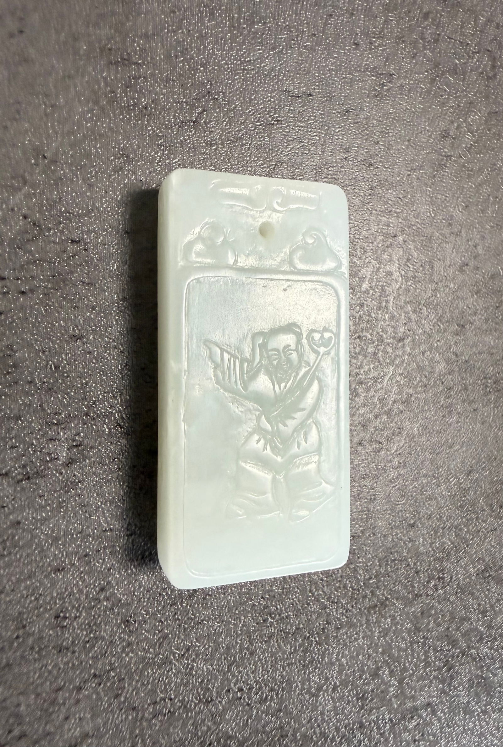 Chinese Carved Jade Pendant Plaque with Boy Motif: A Chinese carved jade pendant plaque featuring a youthful figure carved in relief within a rectangular framed panel. The boy is depicted in a lively pose holding an auspicious object, a traditional
