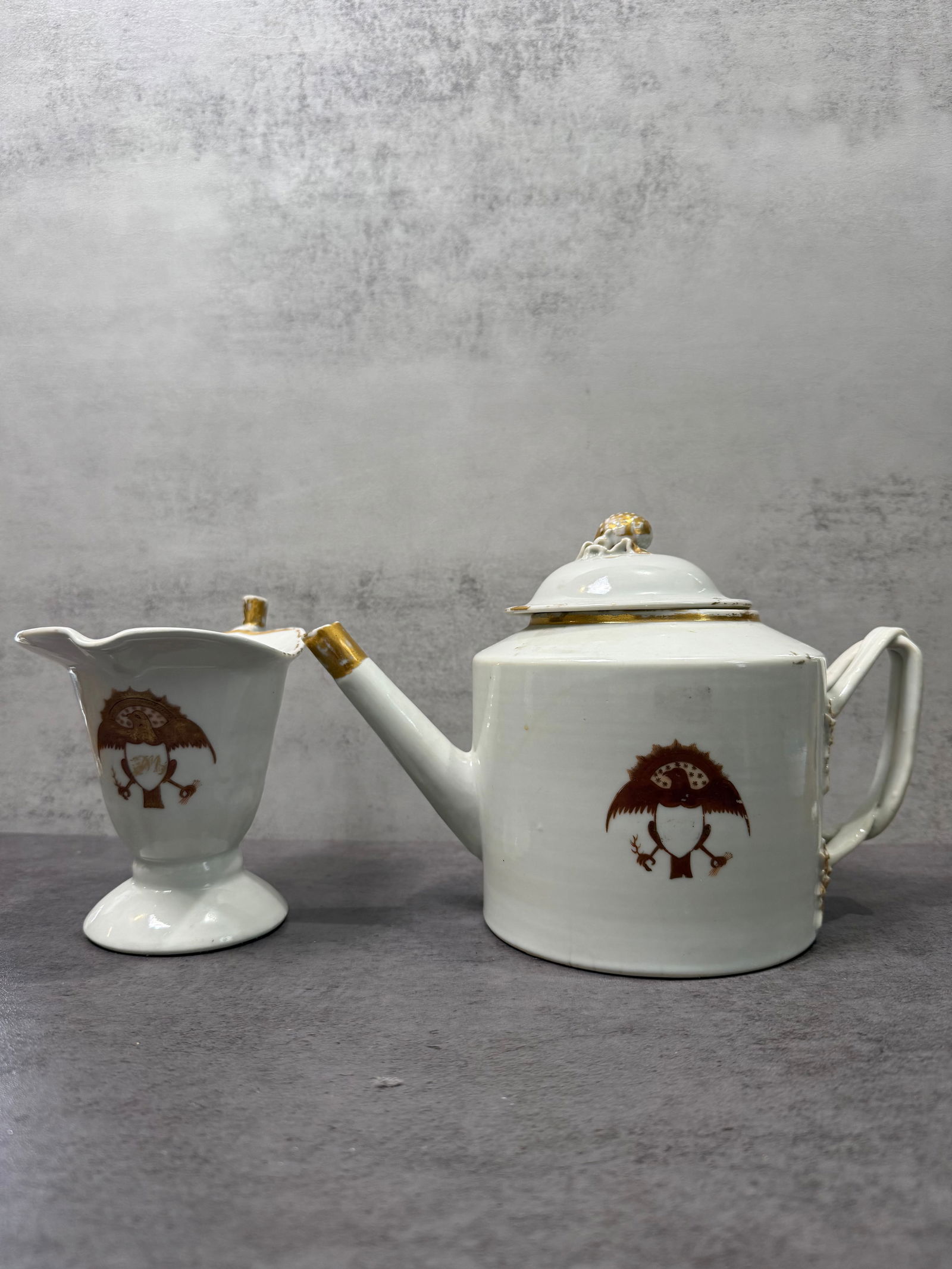 Chinese Export Style Armorial Porcelain Teapot and Creamer: A porcelain teapot and creamer decorated with a heraldic armorial crest motif. The design reflects the tradition of Chinese export porcelain produced for Western markets, where European coats of arms