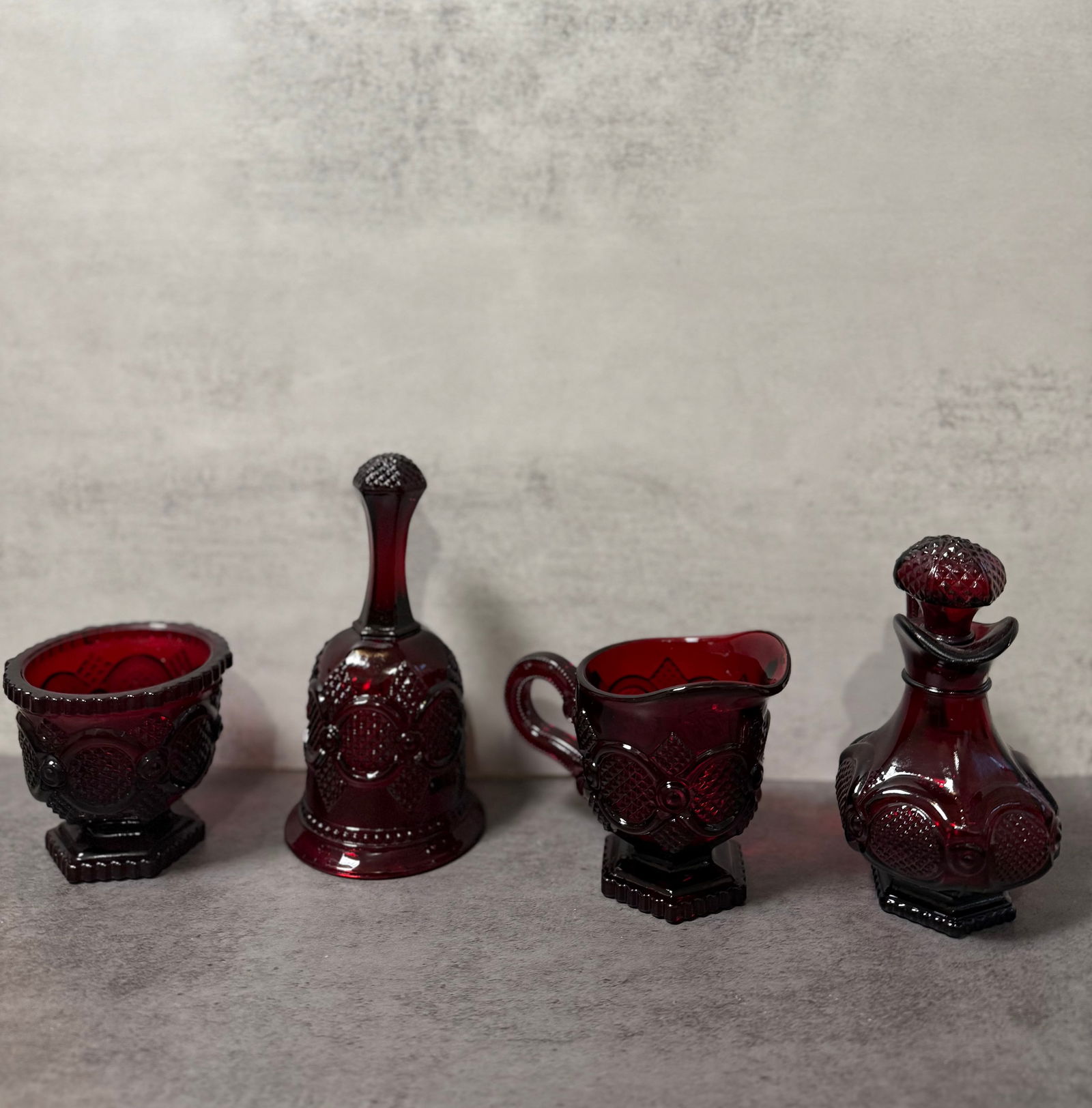 Avon Cape Cod Ruby Red Glass Collection, Bell, Decanter, Creamer & Bowl, Vintage Set: A charming Avon Cape Cod collection grouping in rich ruby red pressed glass, featuring a variety of figural and functional forms including a bell, lidded decanter, creamer, and open bowl.Each piece