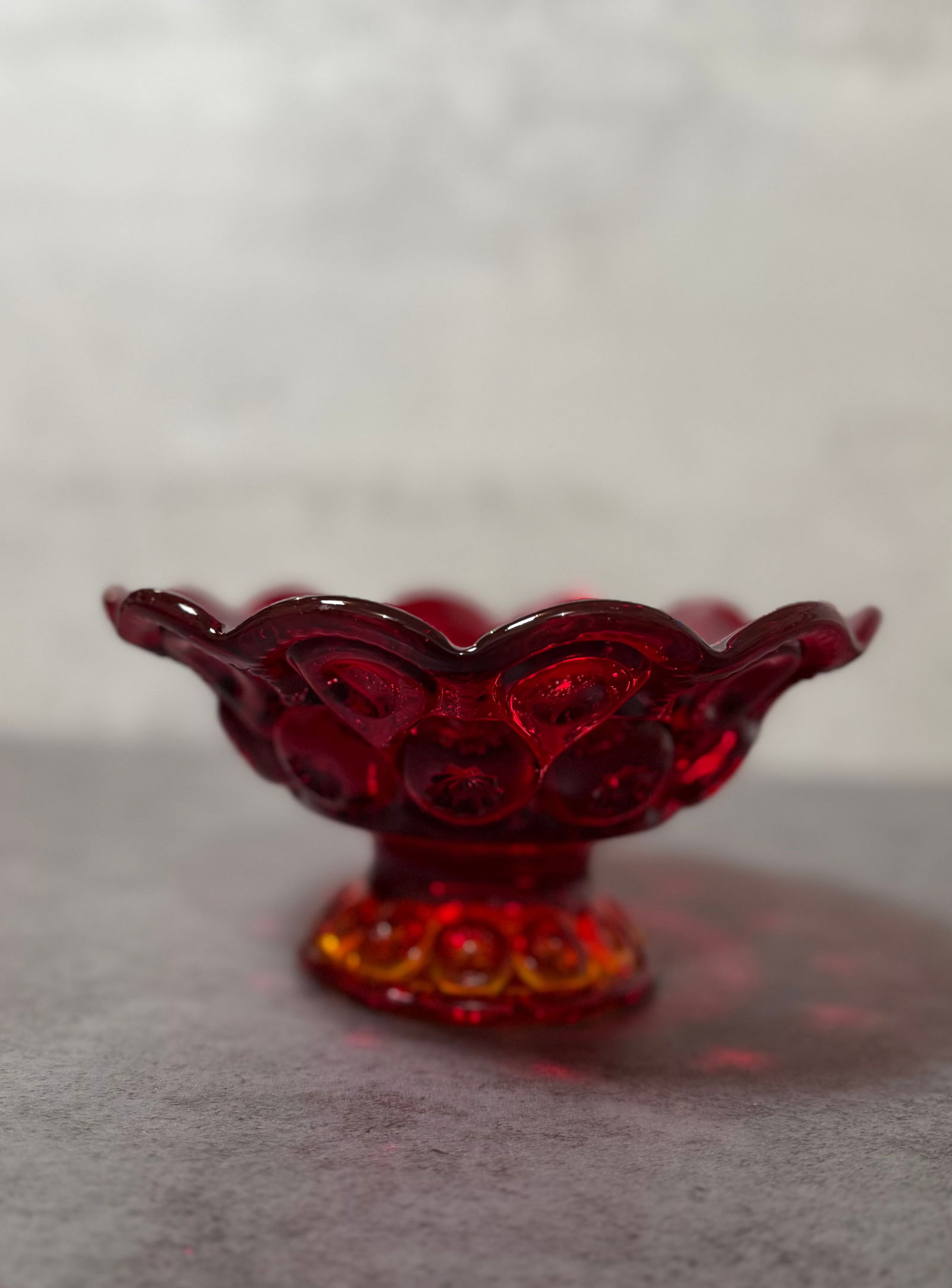 Vintage Ruby Red Pressed Glass Compote, Moon and Star Style Pedestal Bowl: A vintage ruby red pressed glass compote featuring a classic “Moon and Star” style pattern with raised circular and geometric motifs.The bowl is formed with a gently scalloped rim and rests