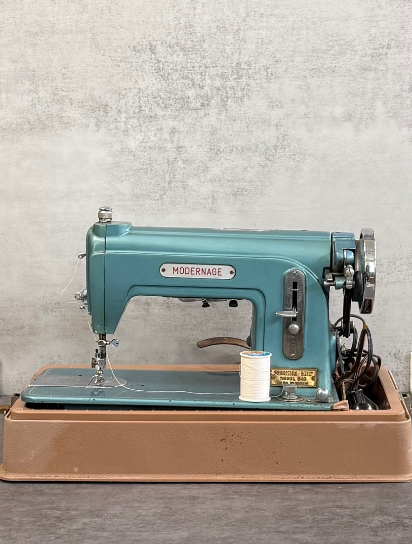 Vintage Modernage Sewing Machine, Portable Electric Sewing Machine with Case: A vintage Modernage portable sewing machine in a classic mid-century design, finished in a distinctive blue tone.This electric machine features a solid metal body, front stitch controls, and comes