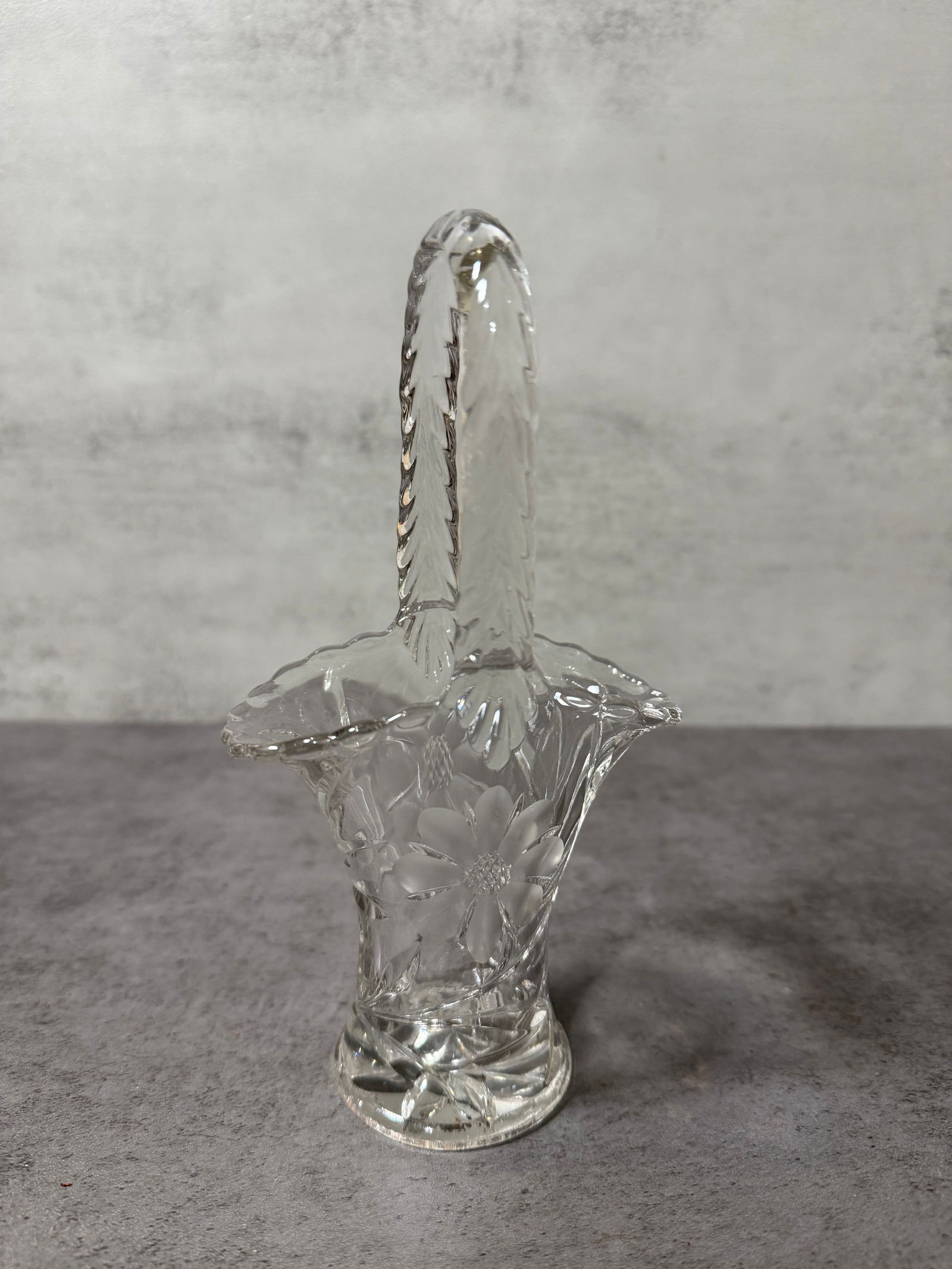 Vintage Cut & Etched Glass Basket with Floral Motif: A vintage decorative glass basket featuring a clear body with etched floral decoration and a faceted handle.The basket form is accentuated by a scalloped rim and a tall upright handle, while the body