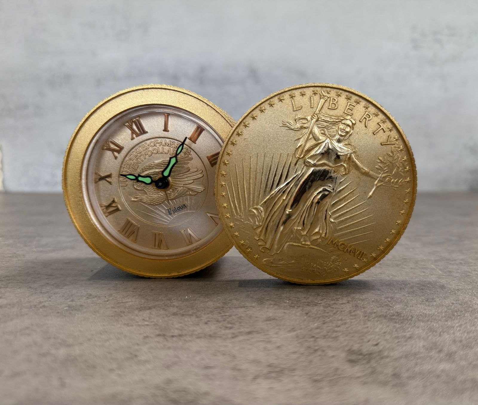 United States Liberty Coin Style Desk Clock – Gold Tone Novelty Timepiece: A distinctive vintage desk clock designed in the form of a United States Liberty coin, featuring a detailed gold-tone finish with iconic imagery.The clock face displays Roman numerals with luminous