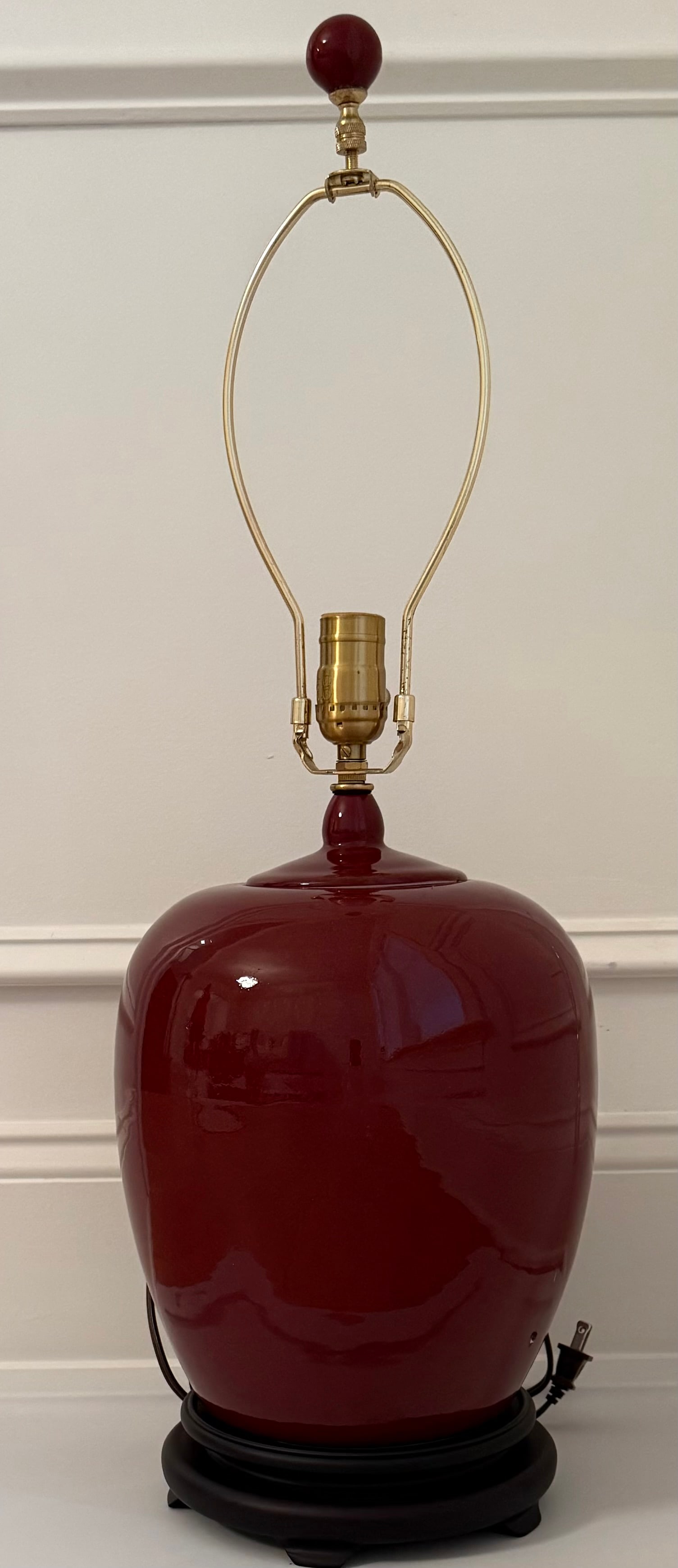 Large Chinese Style Oxblood Red Porcelain Table Lamp: Large porcelain table lamp featuring a baluster-form body decorated in a rich oxblood red glaze. Mounted with brass-tone hardware and raised on a dark wooden base. The lamp displays a clean, elegant s