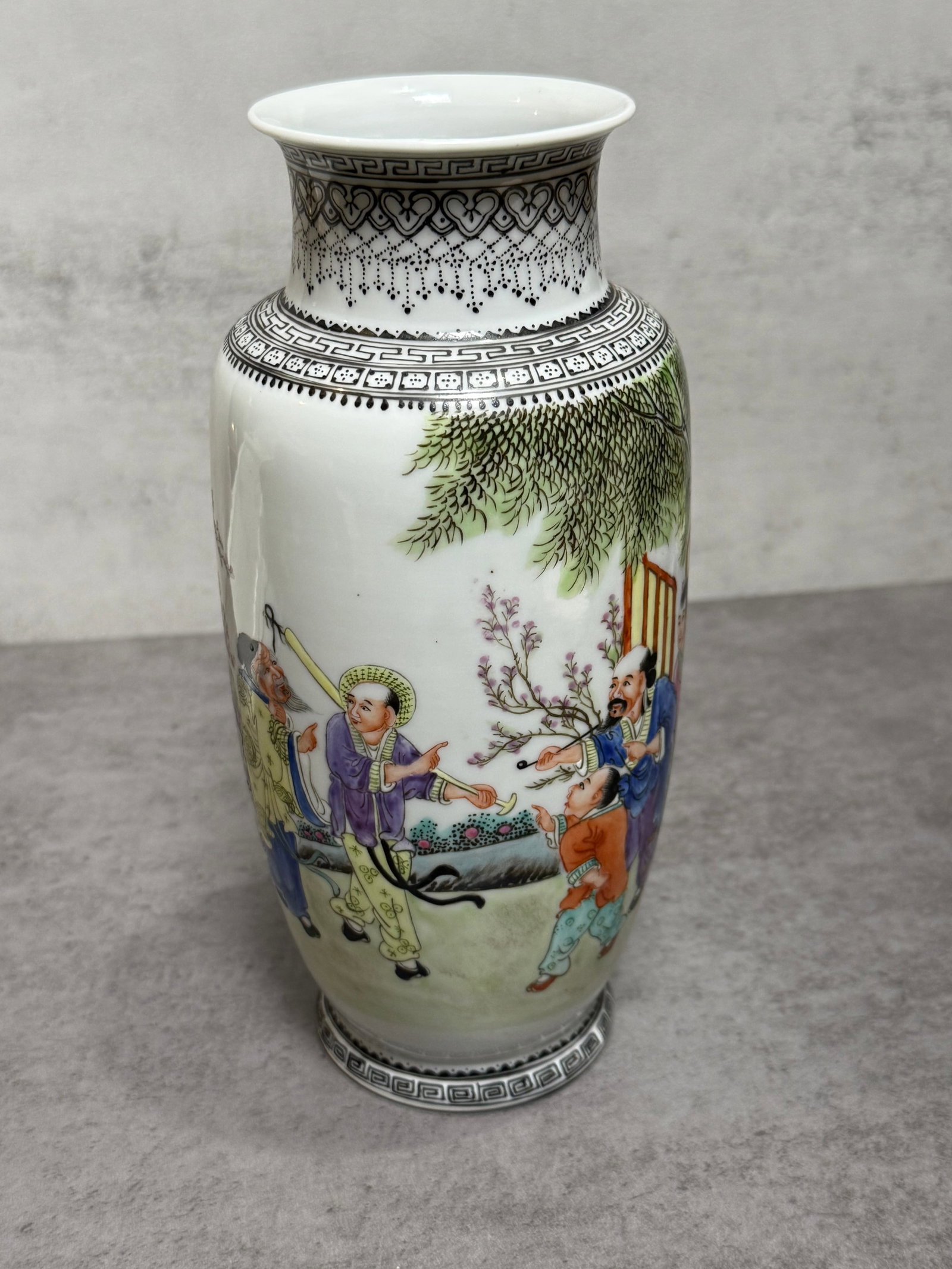 Vintage Chinese Famille Rose porcelain Vase: Chinese porcelain vase decorated in famille rose enamels with a lively figural courtyard scene featuring scholars and attendants beneath trees and flowering branches. The neck and borders are