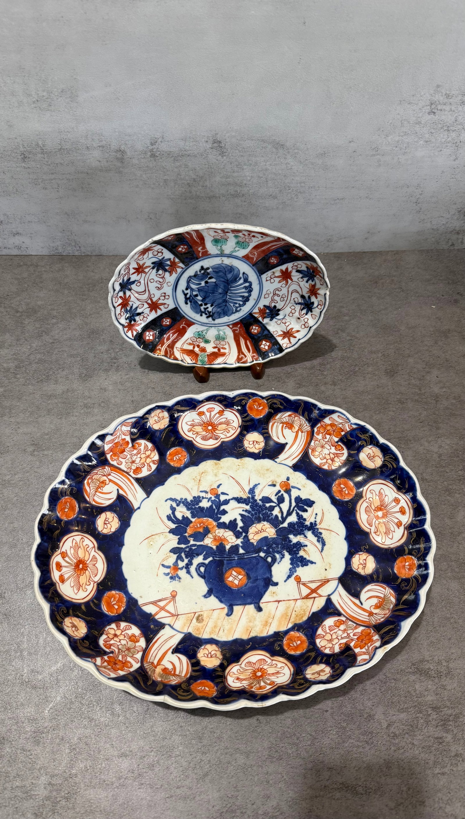 Group of Japanese Imari Porcelain Plates With Floral Motifs: A decorative group of Japanese Imari porcelain plates featuring cobalt blue, iron-red, and gilt decoration. The larger scalloped-edge charger is centered with a floral urn arrangement surrounded by