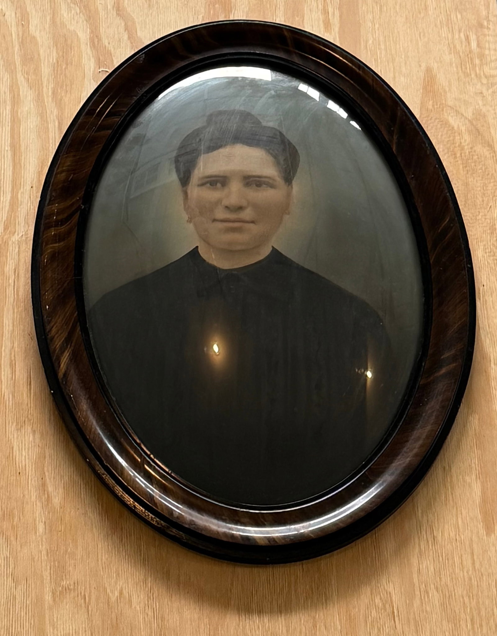 Antique Oval Framed Portrait Photograph of Woman under Convex Glass: An antique portrait photograph depicting a seated woman in dark attire, presented in an oval wooden frame with convex bubble glass. The image displays the soft tonal quality and solemn presentation