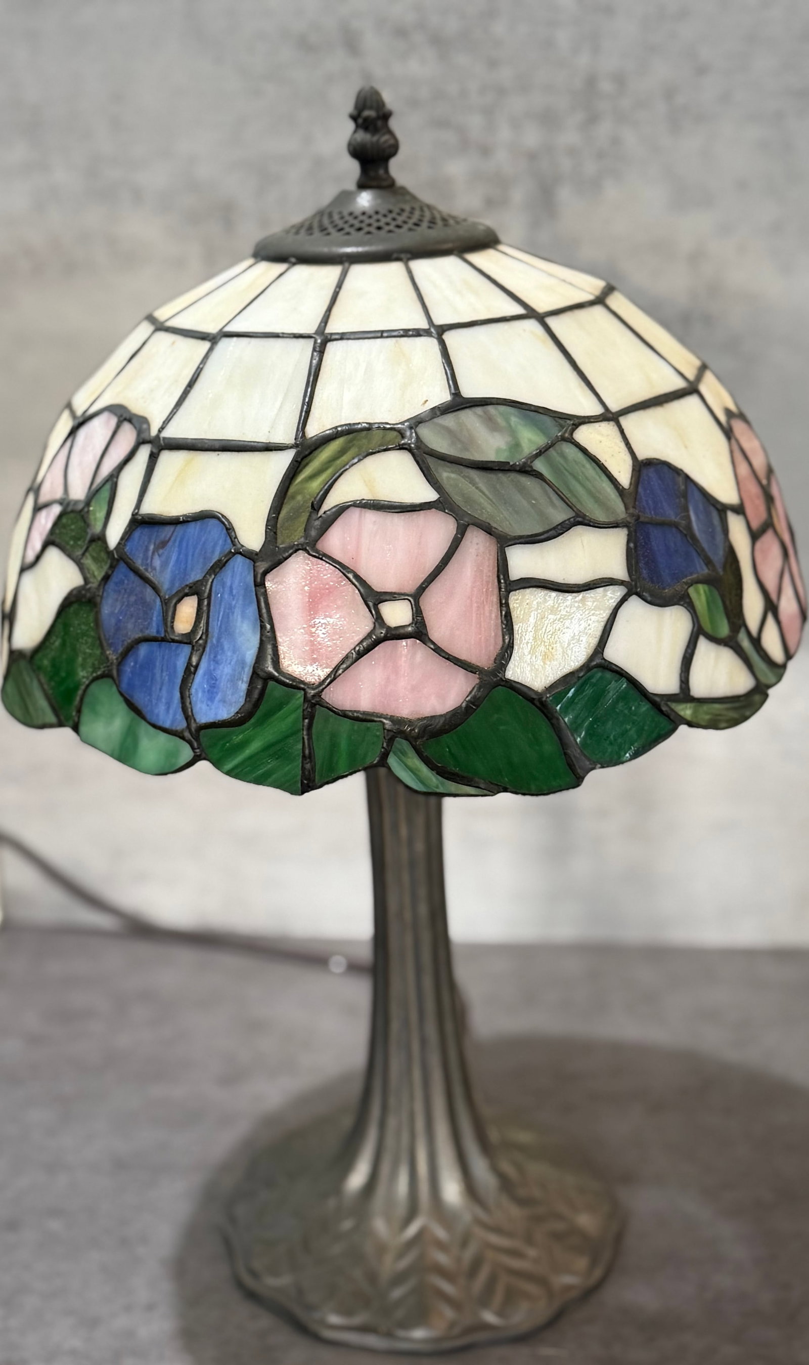 Vintage Tiffany Style Floral Leaded Glass Table Lamp: Vintage Tiffany-style table lamp featuring a leaded stained glass shade decorated with stylized floral motifs in pink, cobalt blue, and green tones set against an opalescent cream ground. The domed