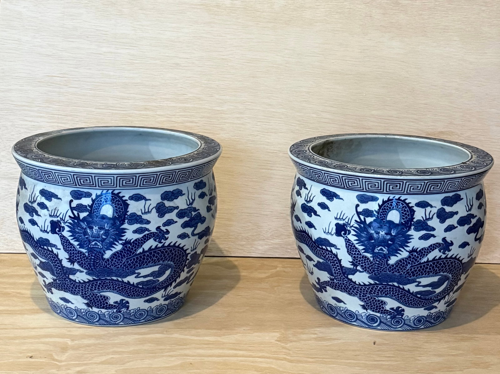Pair of Large Chinese Blue & White Dragon Porcelain Planters: Pair of large Chinese blue and white porcelain planters decorated with fierce five-clawed dragons soaring amidst scrolling clouds above stylized wave borders. Each planter features a broad mouth with