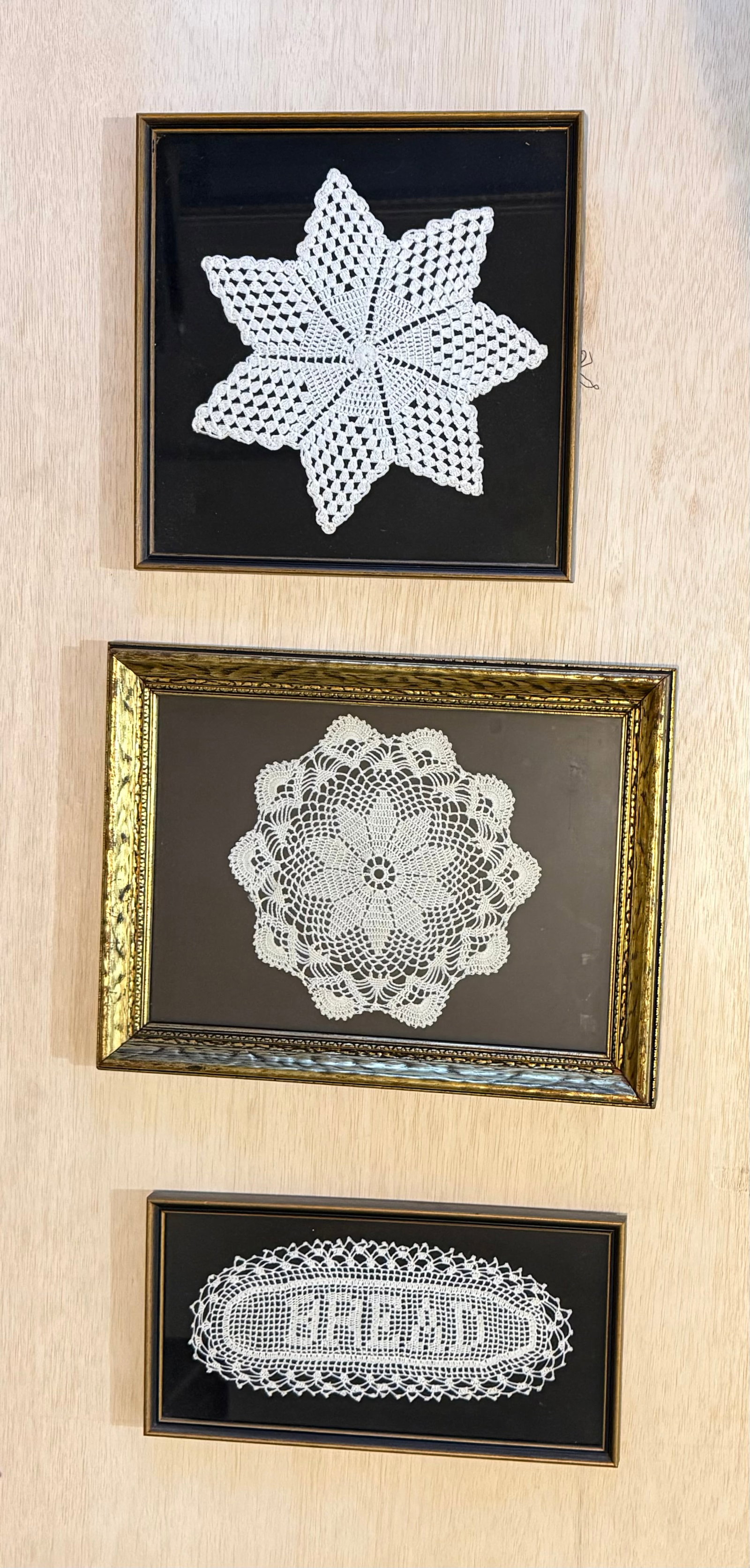 Three Framed Hand-Crocheted Lace Doily Wall Hangings: Collection of three framed hand-crocheted lace doily panels displayed against contrasting dark grounds within decorative frames. The group includes a star-form example, a floral medallion design, and